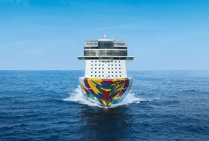 A large Norwegian Encore cruise ship sailing on a calm blue ocean