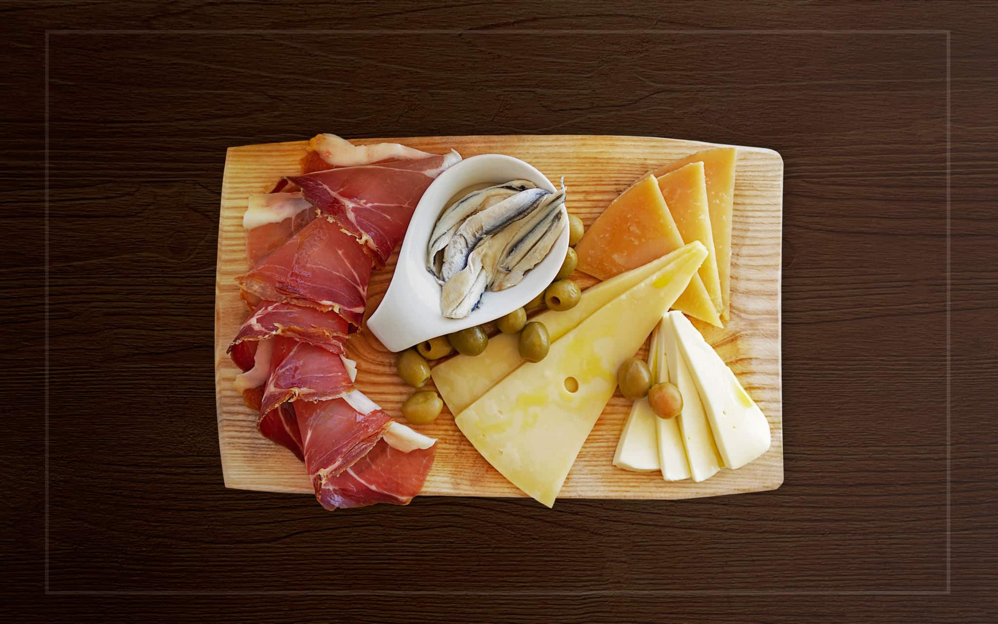 Croatian traditional food, Dalmatian plate. Proshut, cheese sprinkled with olive oil with capers in a pickle with olives on a wooden dish on a background with a frame.The perfect appetizer for wine
