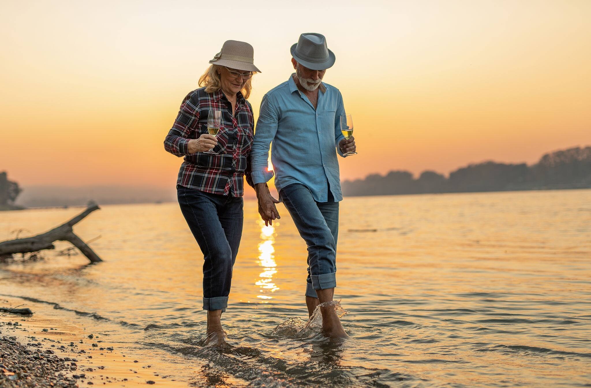 Portrait of a happy senior couple drinking wine and enjoying the sunset on the river.	