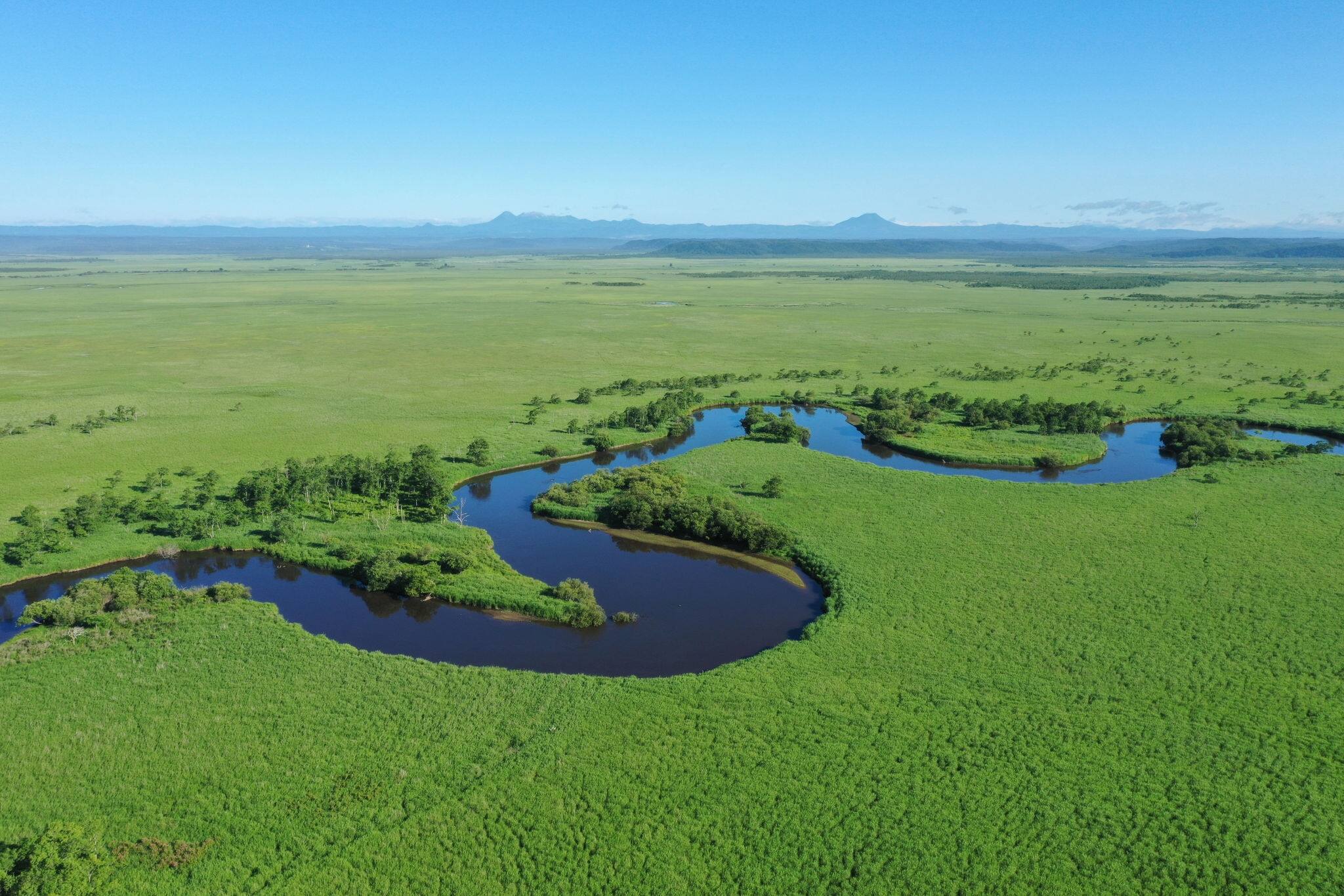 Kushiro River flowing through the Kushiro Marsh in summer in eastern Hokkaido Drone aerial photography Mt. Meakan Mt. Oakan