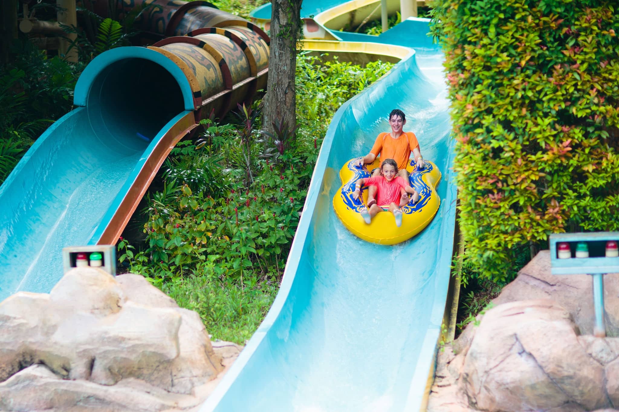 Kids on water slide in outdoor swimming pool. Family in aqua theme park. Children have fun in splash playground. Summer vacation with child. Kid on inflatable tube sliding into a pool.