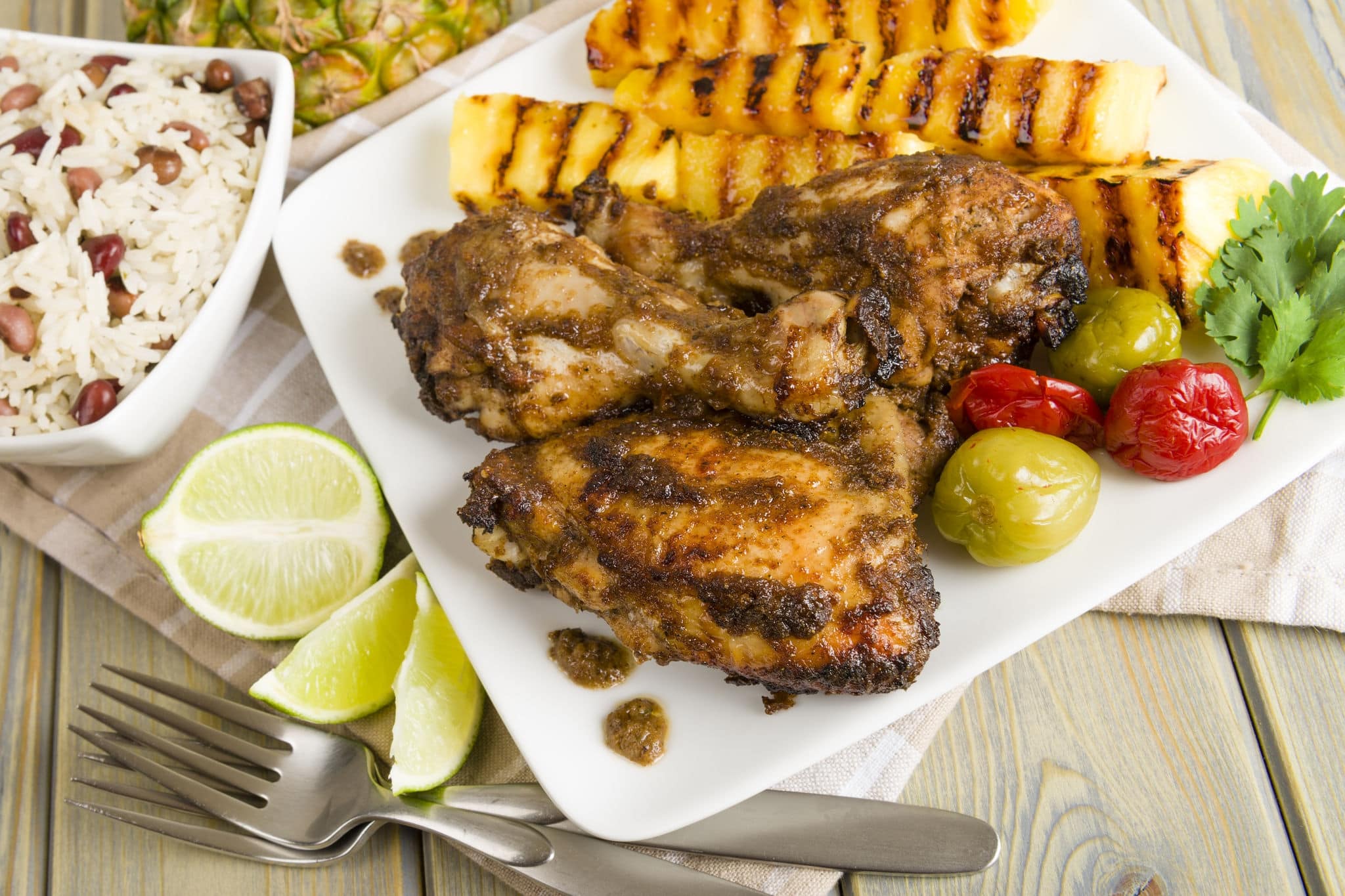 Jerk Chicken - Jamaican marinated BBQ chicken served with grilled pineapple, rice and peas and lime wedges.