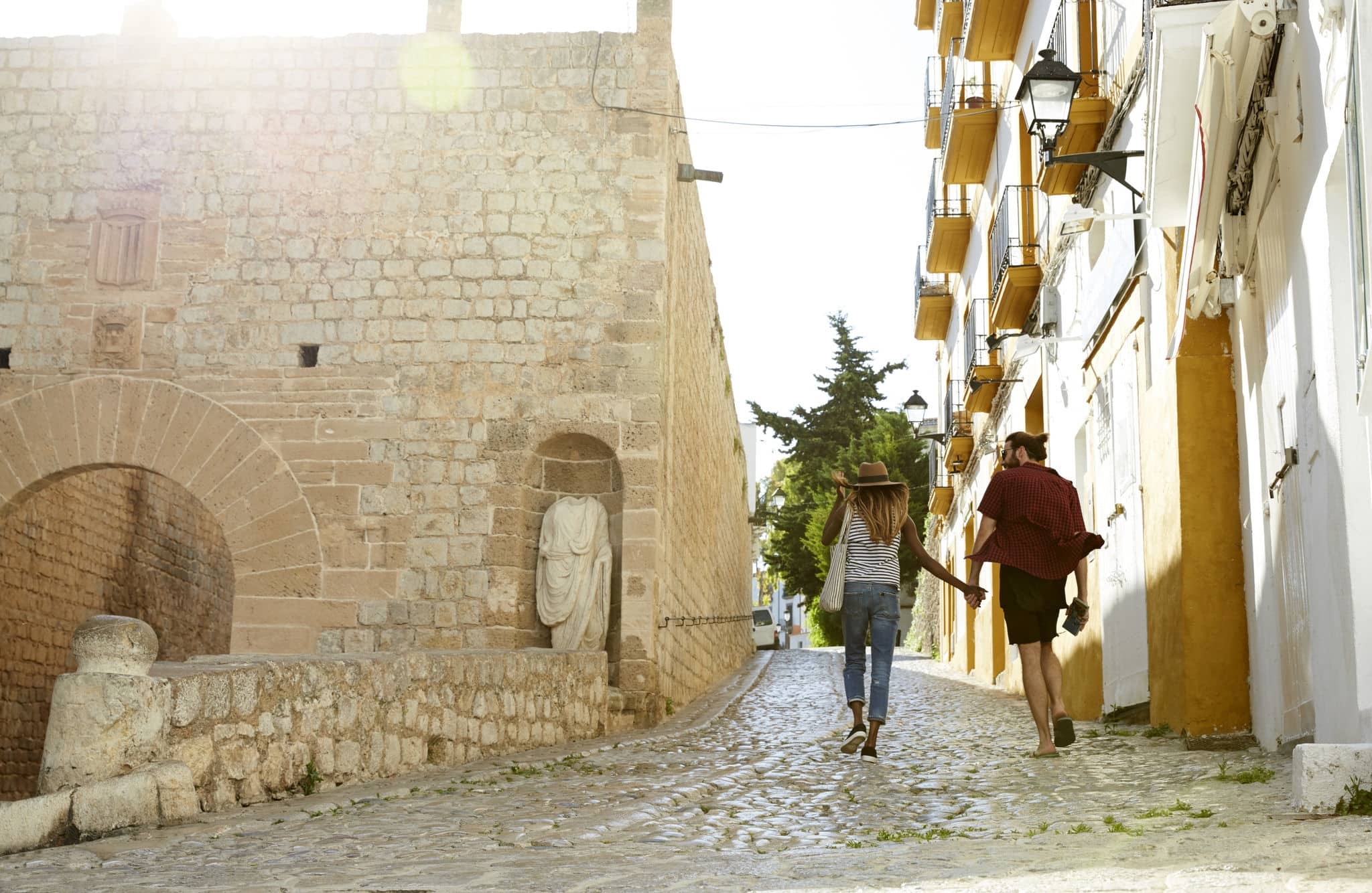Couple on holiday hold hands walking in Ibiza, back view