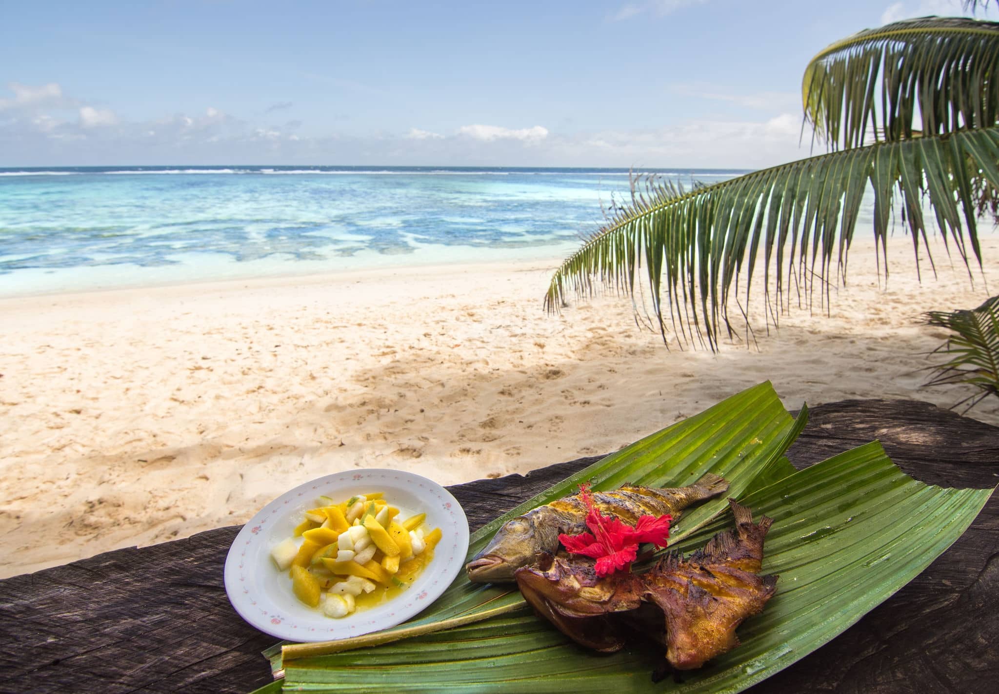 Plate of creole food with fish and mango salad on Seychelles Islands, Anse Source D'argent beach / Red Snapper fish with mango salad on a palm tree leaves, traditional creole food