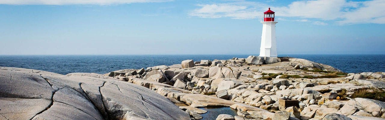 Peggy's Point Lighthouse in Nova Scotia Canada with blue sky and rocks in foreground
