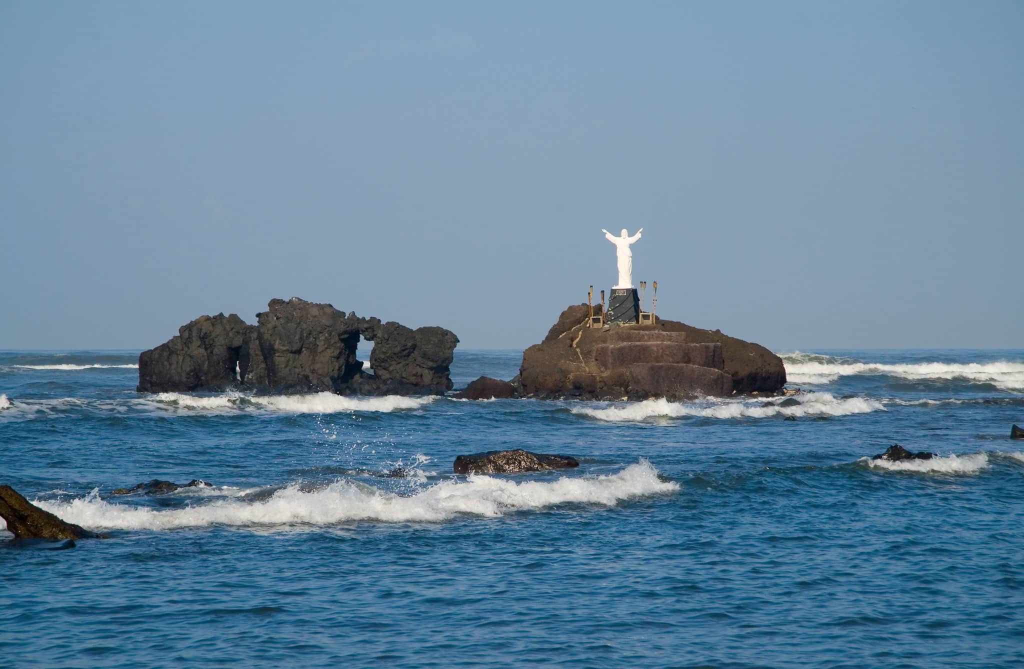 A statue of Jesus stands on a small island of volcanic rocks