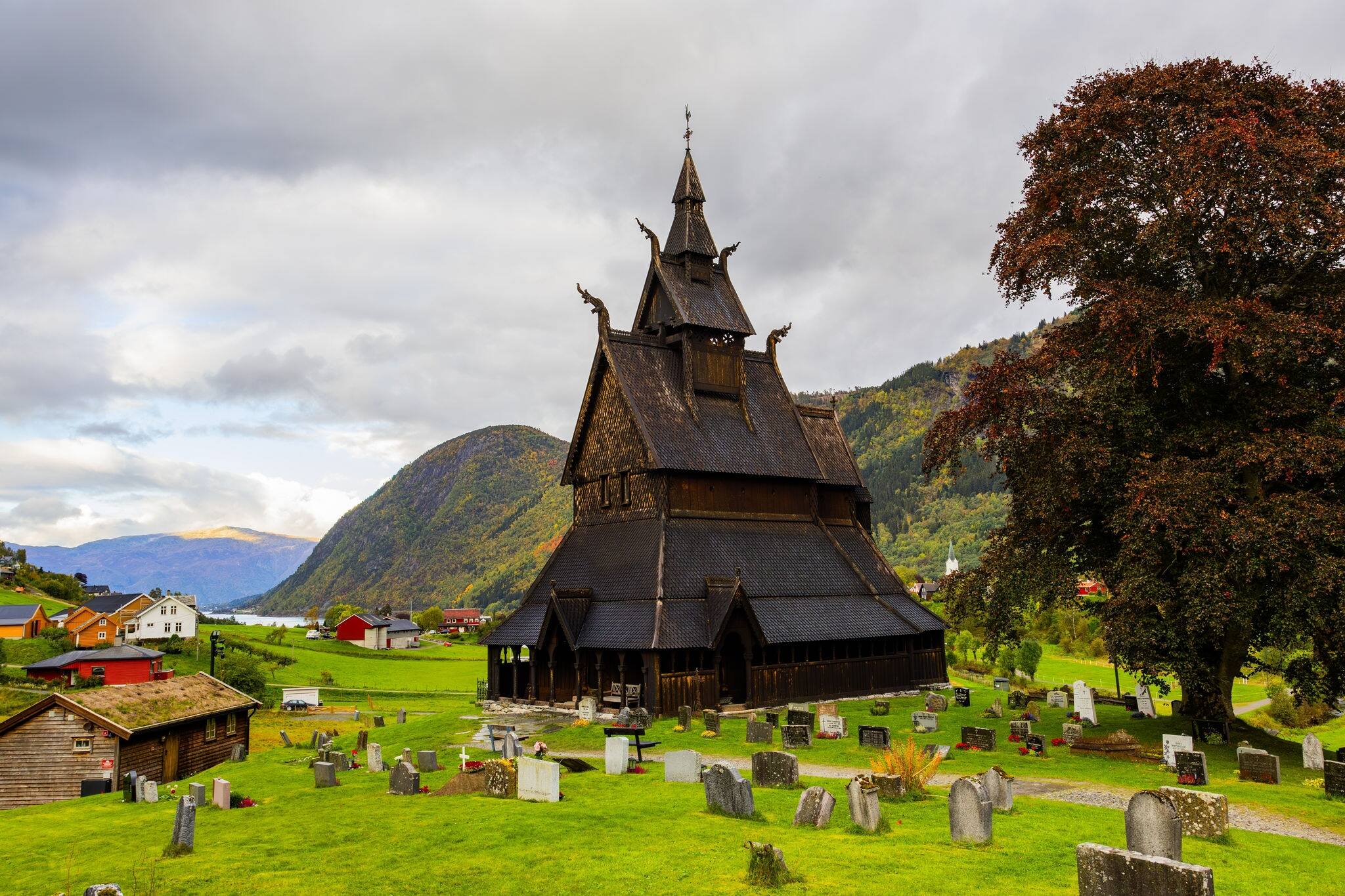Hopperstad Stavkyrkje in Norway, a historic wooden church surrounded by autumn trees and a peaceful graveyard.