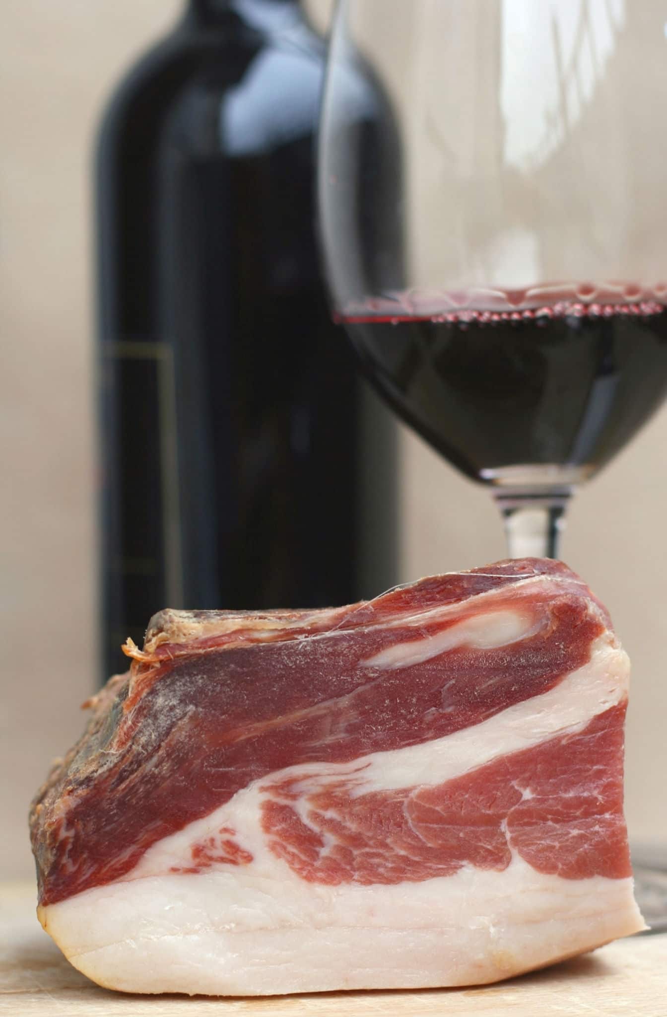 Typical Slovenian dry cured smoked ham called prsut from Slovenia with red wine in background