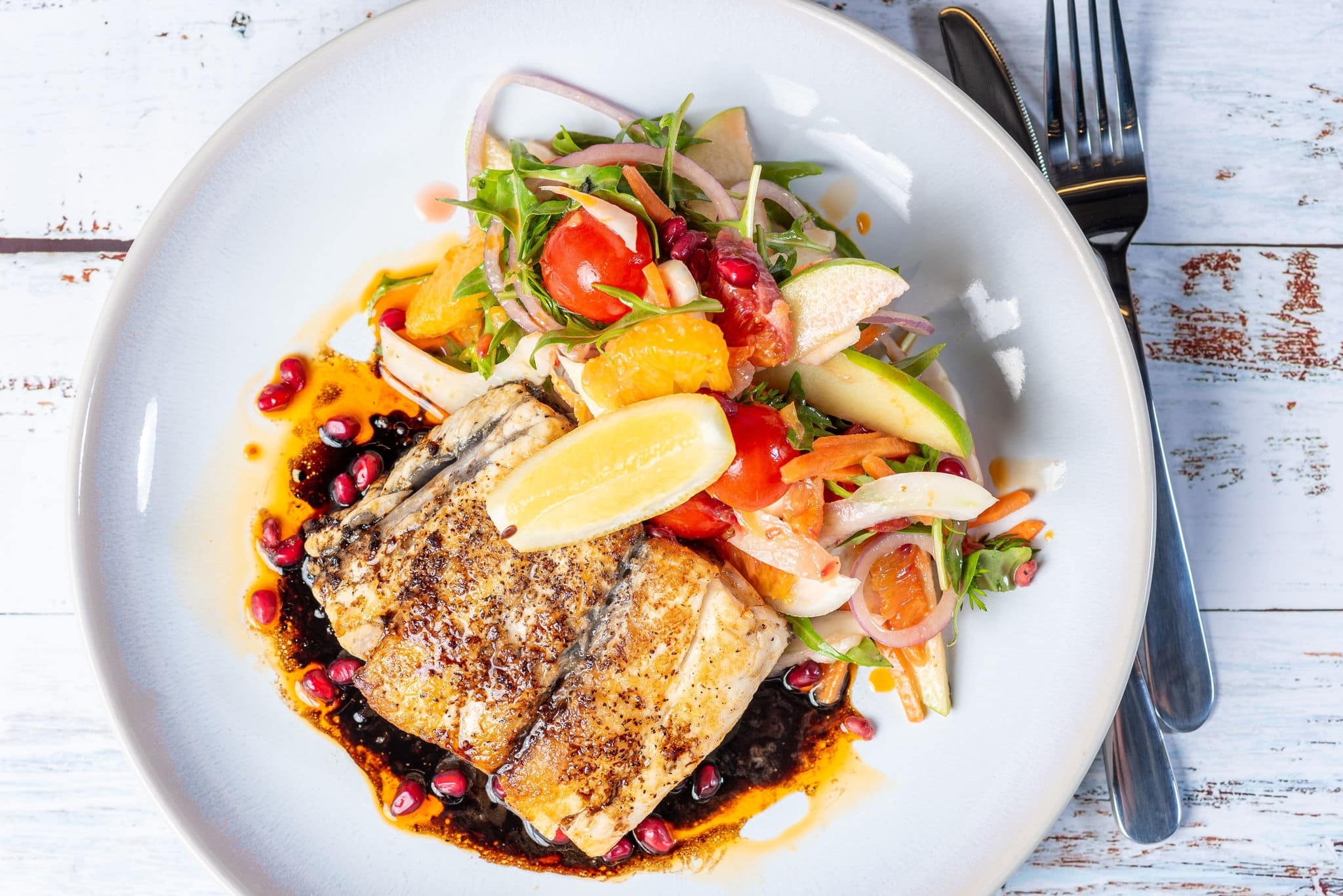 Grilled Barramundi with a side of salad, served on a white round plate with knife and fork.