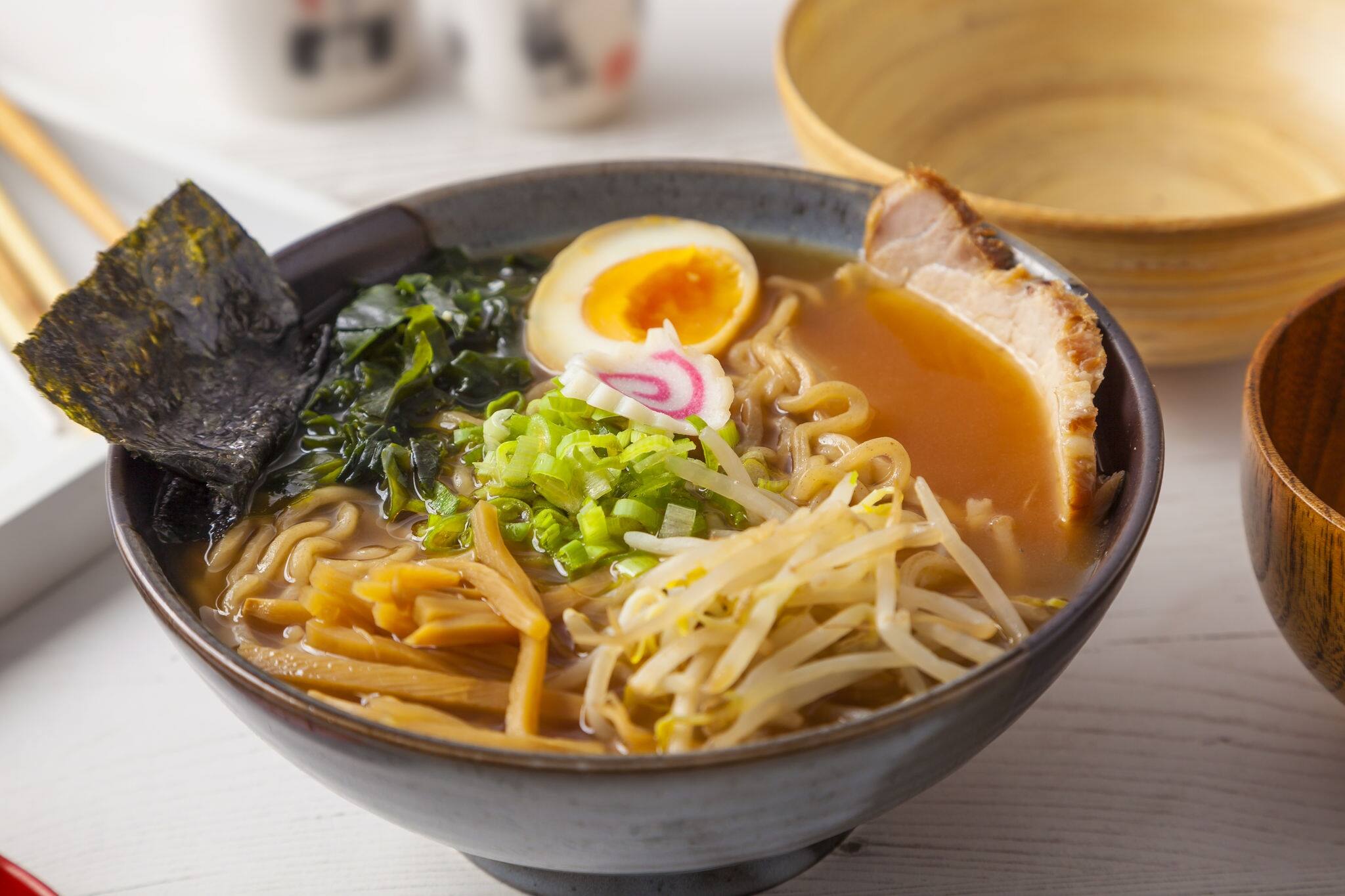 Miso Ramen Asian noodles with meat and egg in bowl on white wooden background.