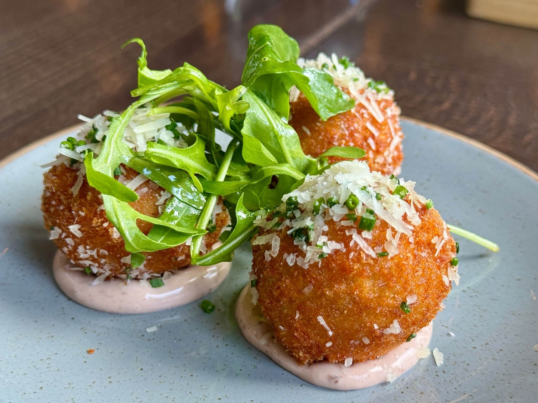 Close-up of Crispy Arancini Balls Topped with Fresh Arugula and Grated Parmesan