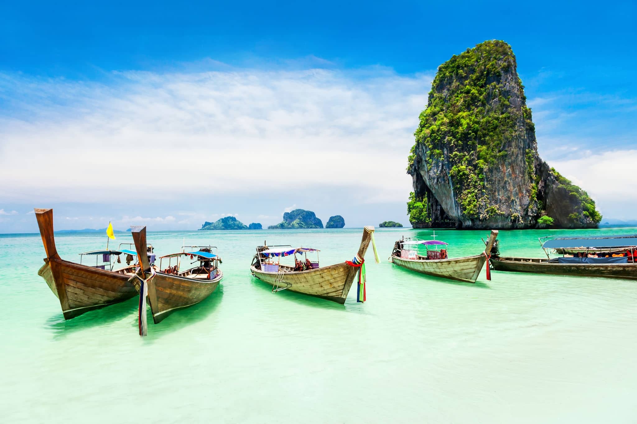 Longtale boats at the Phuket beach with limestone rock on background in Thailand. Phuket island is a most popular tourist destination in Thailand.