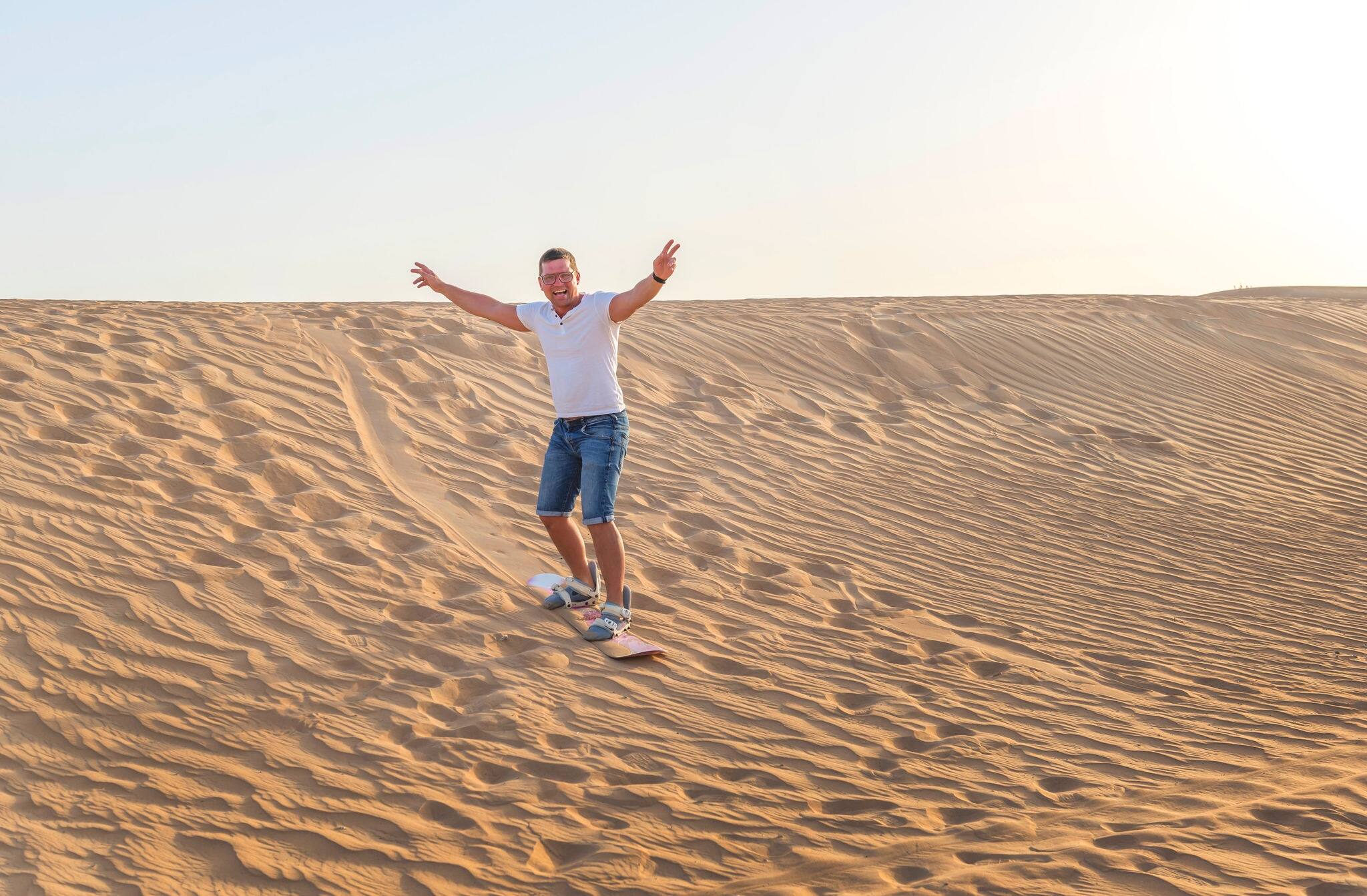 Man sand boarding in a desert down the dune near Emirates. Dubai, UAE.