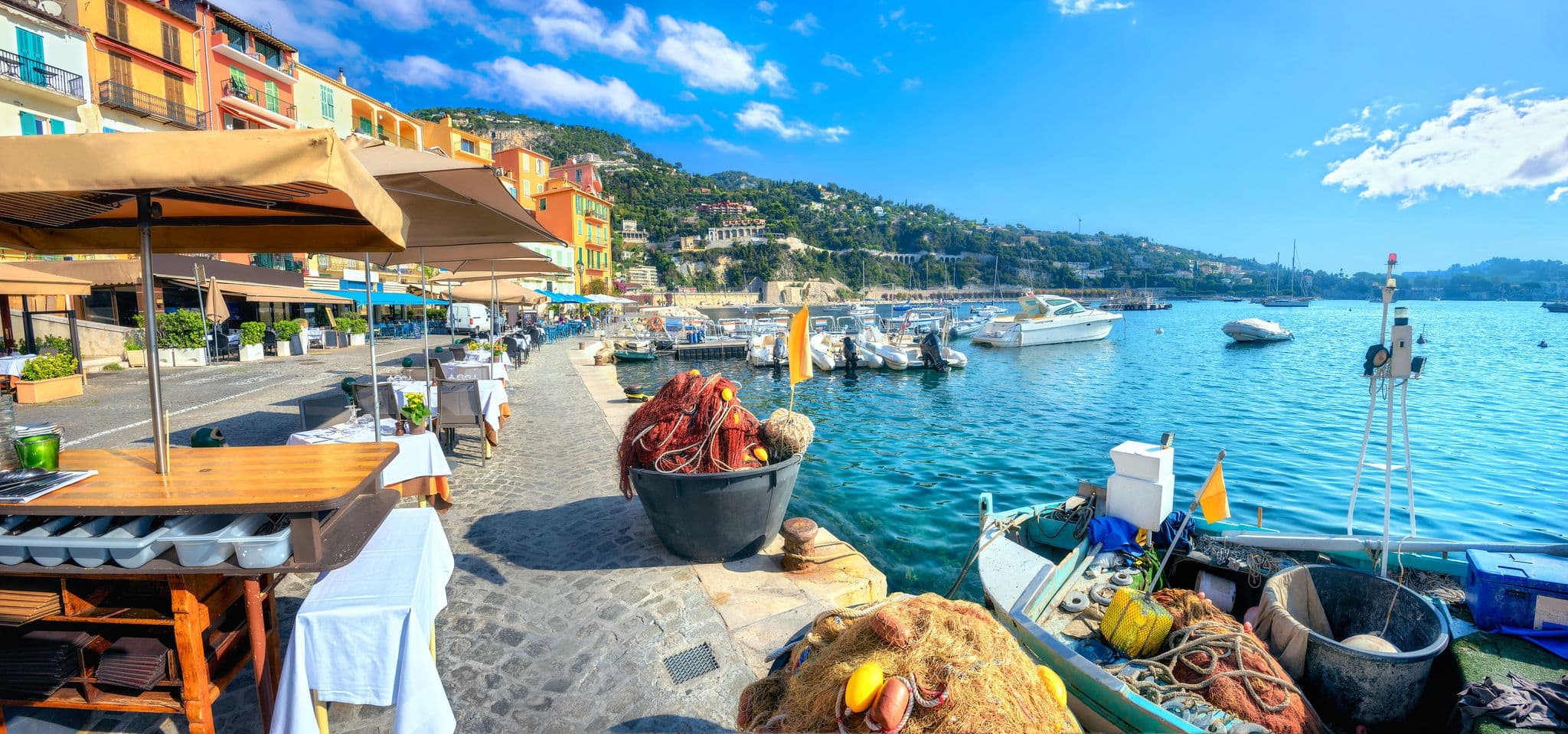 Panoramic cityscape with street cafe and fishing boat  in resort town Villefranche sur Mer. Cote d'Azur, France    