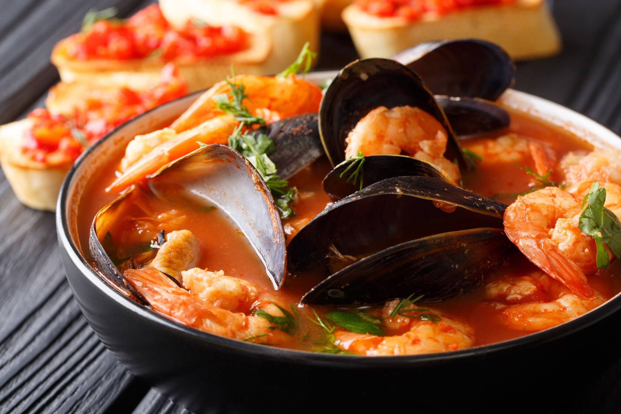 Freshly cooked seafood bouillabaisse soup with shrimps, fish fillets and mussels closeup in a bowl on the table. horizontal