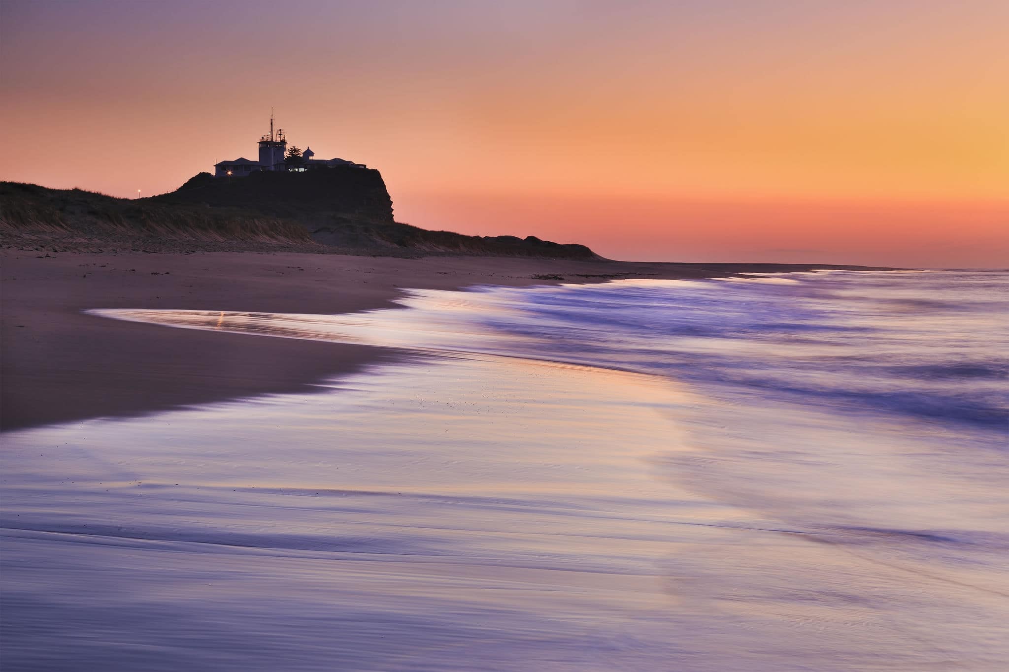 Nobbys lighthouse in Newcastle of Australia at sunrise sinking in warm pink rays of rising sun