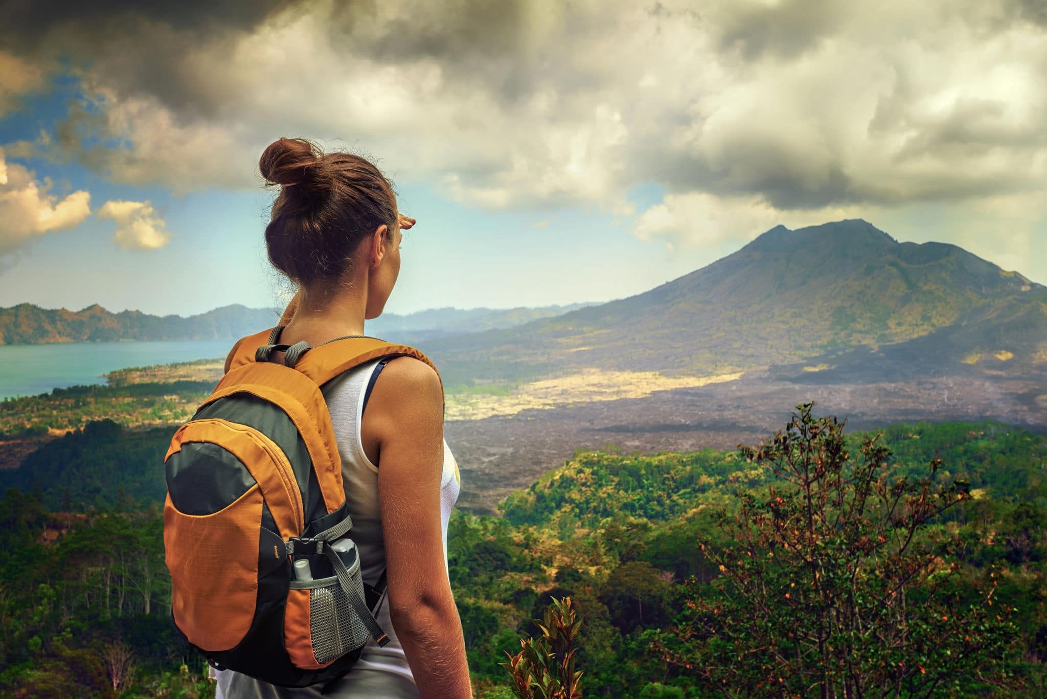 Lady tourist with a backpack standing on top of the mountain and enjoy the beautiful volcano Batur. Indonesia