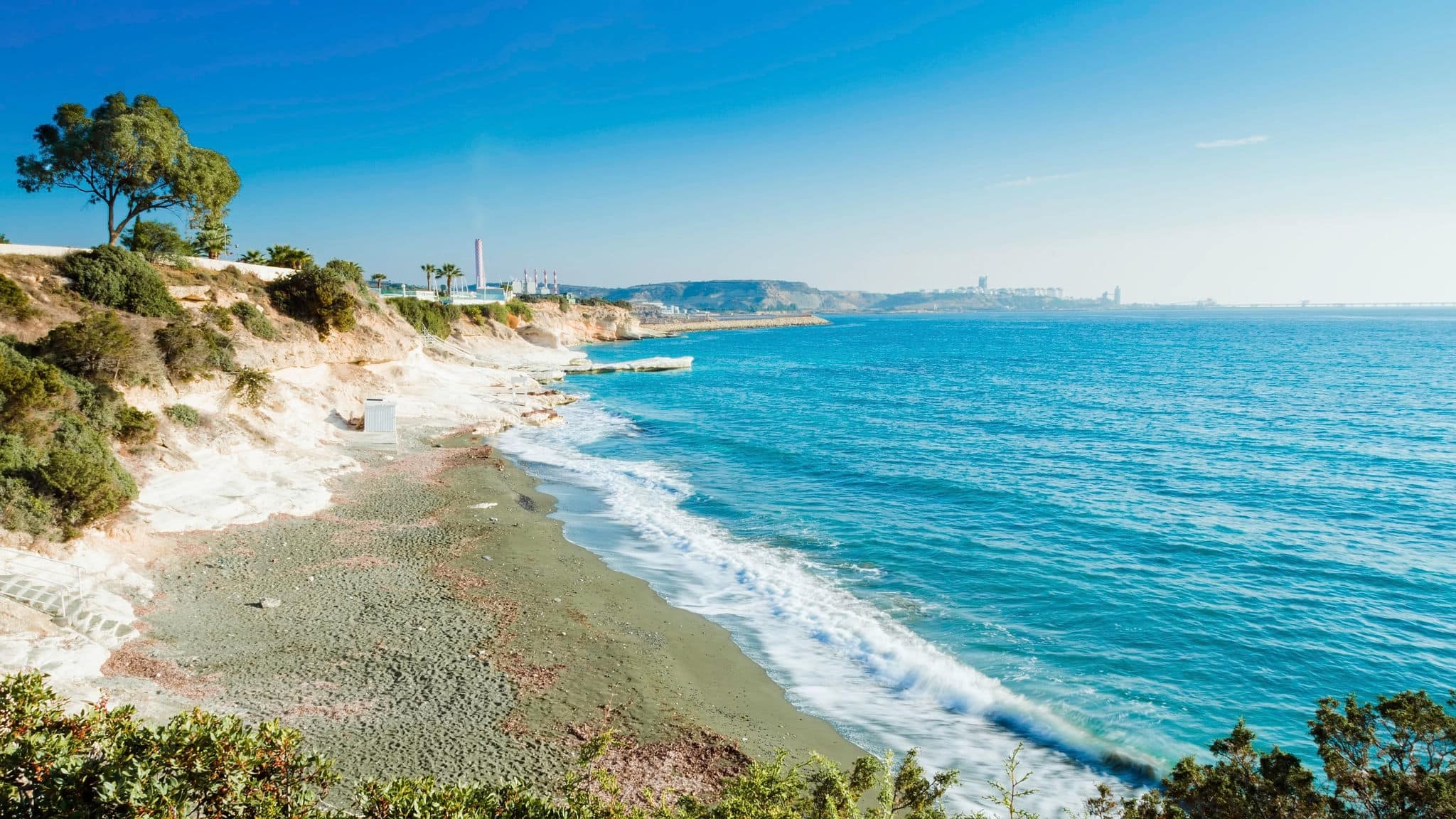 The coastline and landmark big white chalk rock at Governor's beach, Limassol, Cyprus. Steep stone cliffs and deep blue sea waves crushing in coves and dark sand next to Vasilikos power station.