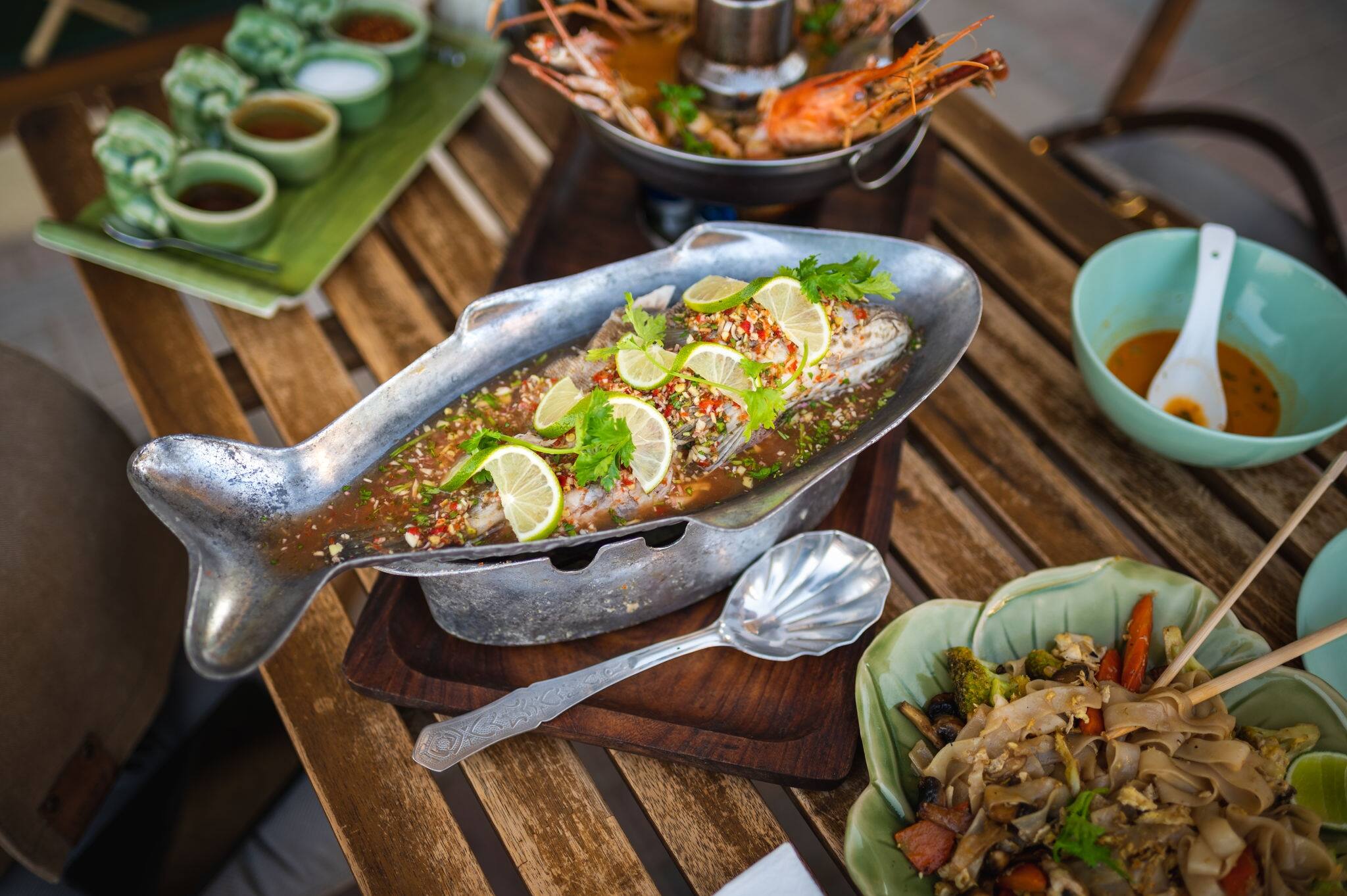 Steamed hammour fish with lime pepper and various food ingredients on a table with Thai food dishes