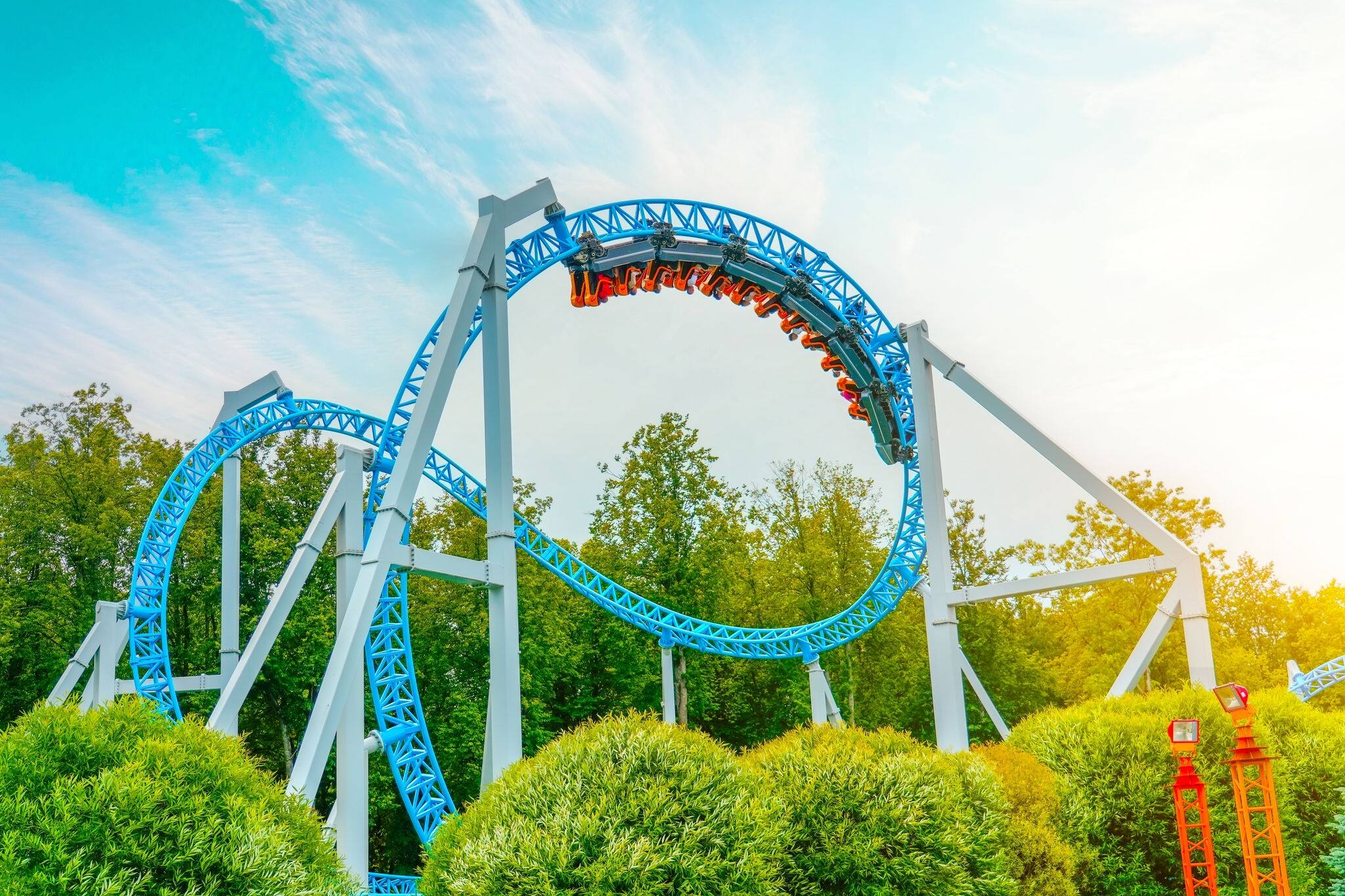 Roller coaster cart with people riding it goes through a loop upside down in green trees bushes city park. Loop metal frame of a roller coaster in an amusement park