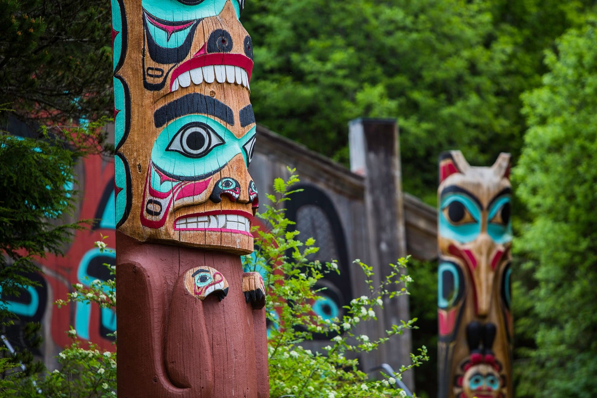 Detail of totem pole at Saxman Village tribal house near Ketchikan Alaska with Sun Raven in background