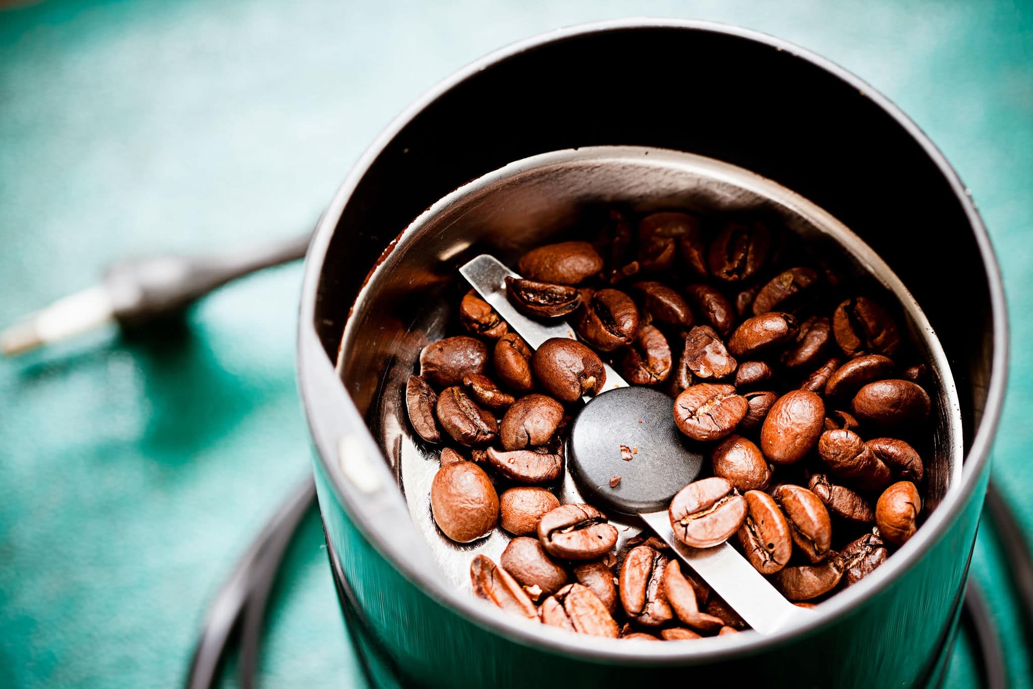 Electric coffee-mill machine with roasted coffee beans on the kitchen table with green tabletop