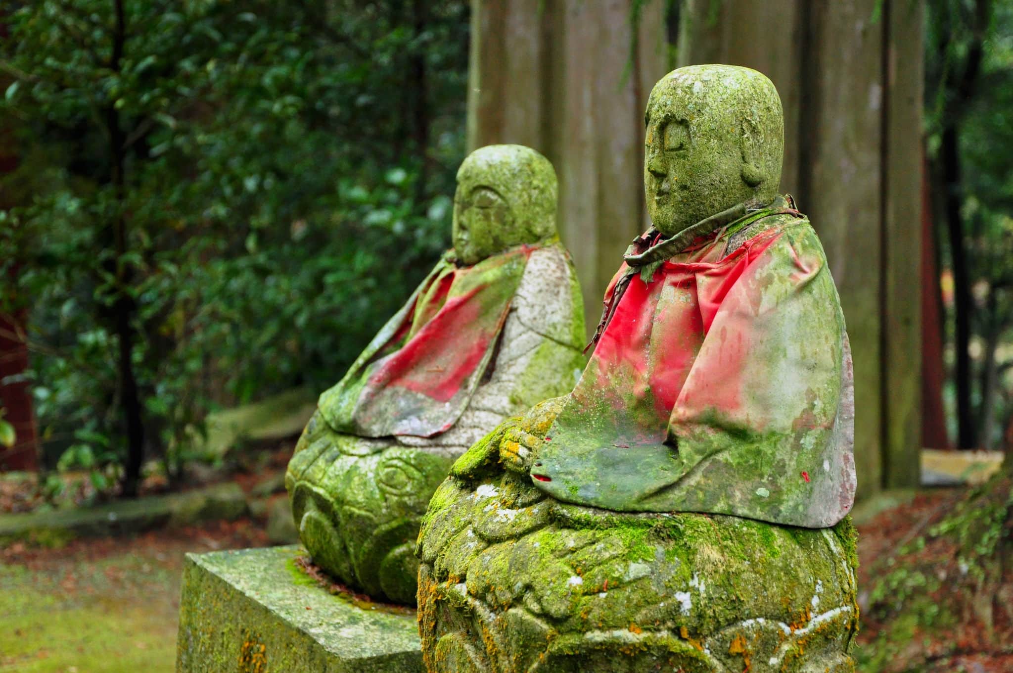 Old mossy green Jizo (Bodhisattva) statues with red cloak near small temples on Mount Shosha, Himeji, Japan