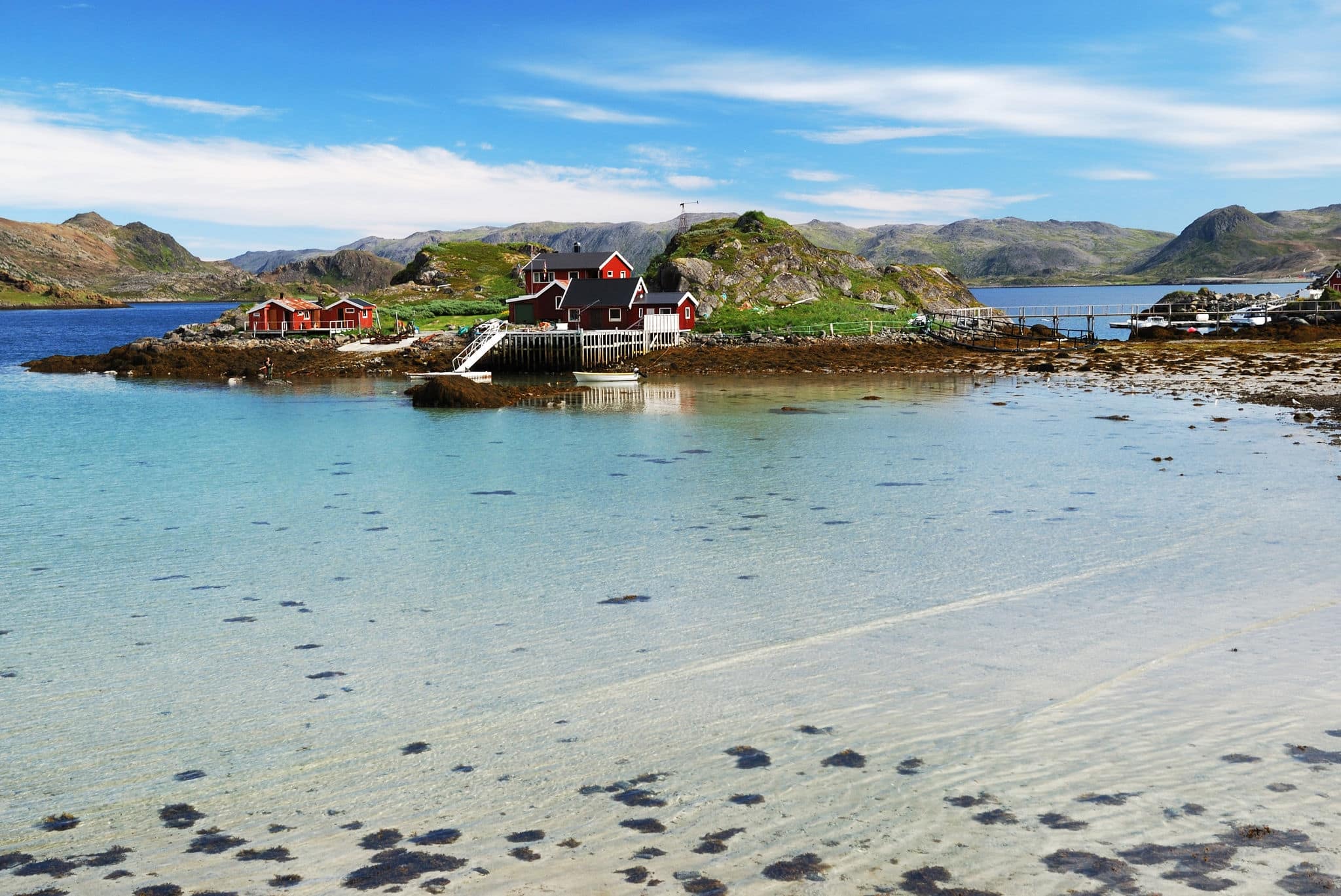 Fishing village is in the small island surrounded with blue fjord during low tide in summer. There are several wooden houses, motorboats, mossy hills and a lot of transparent water.