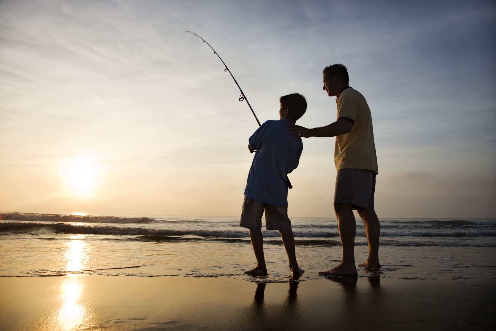 Father and son fishing in ocean surf at sunset.