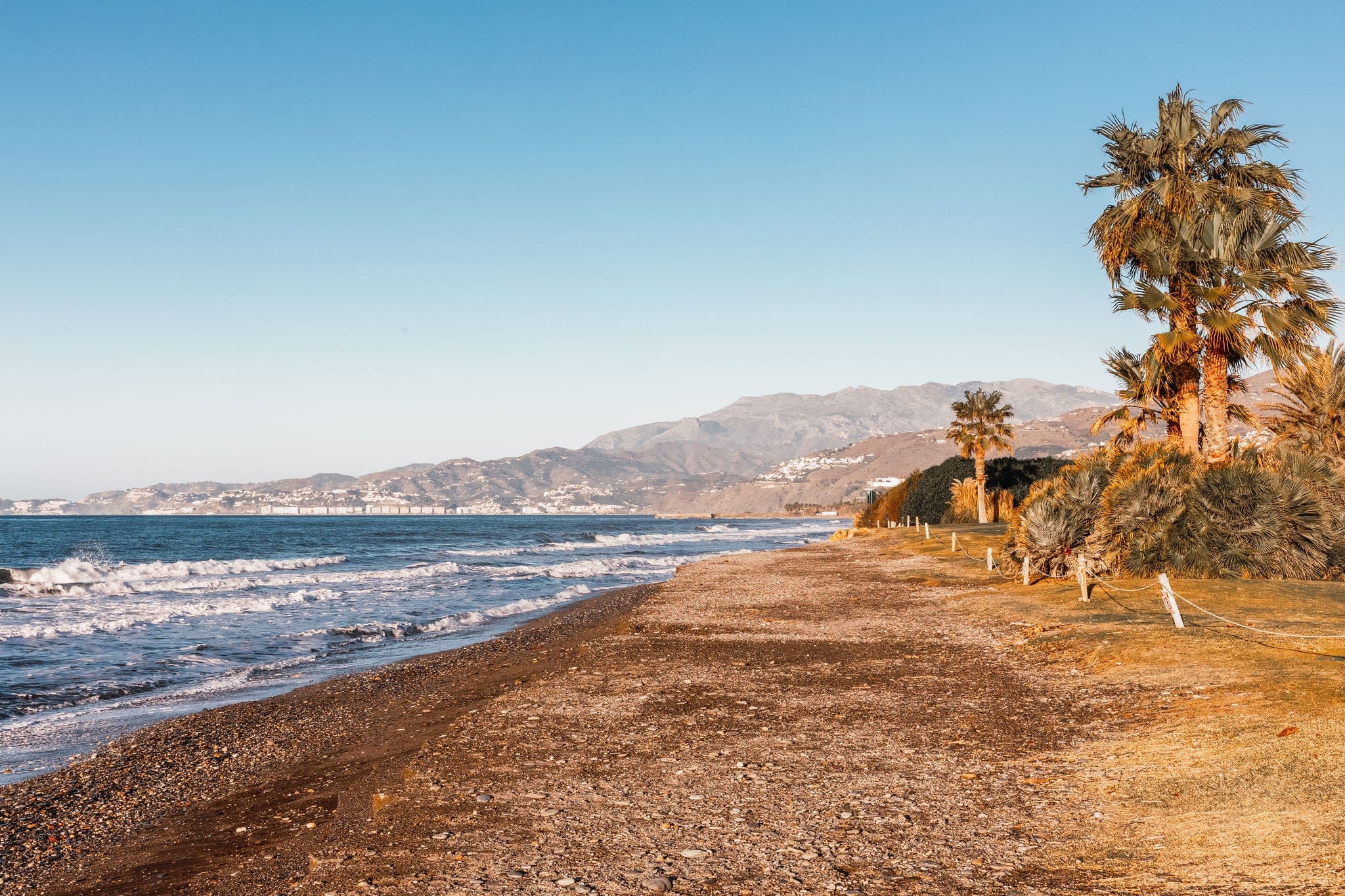 Uncrowded paradise beach in Motril, in the south of Spain with blue sea, waves, palm trees and mountains in the background.
