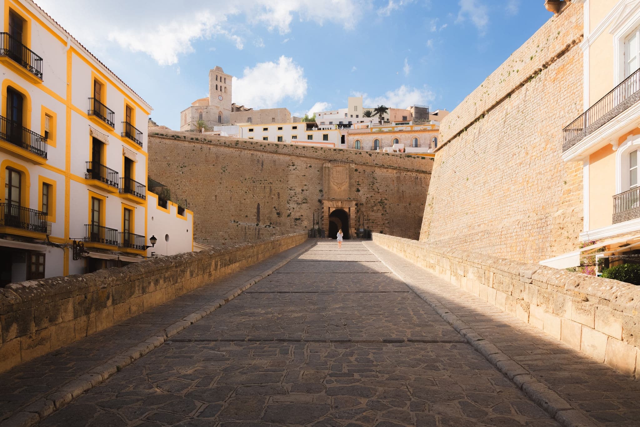 A young blonde female tourist approaching the fortified walls and Castle of Ibiza, in the historic old Ibiza Town, in the Spanish Balearic Islands on a sunny, summer day.