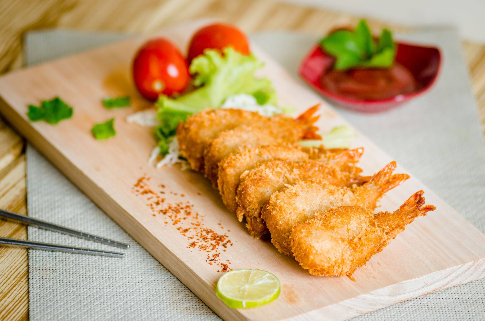 Butterfly ebi furai shrimp served with tomato and lettuce on a wooden chopping board along with ketchup
