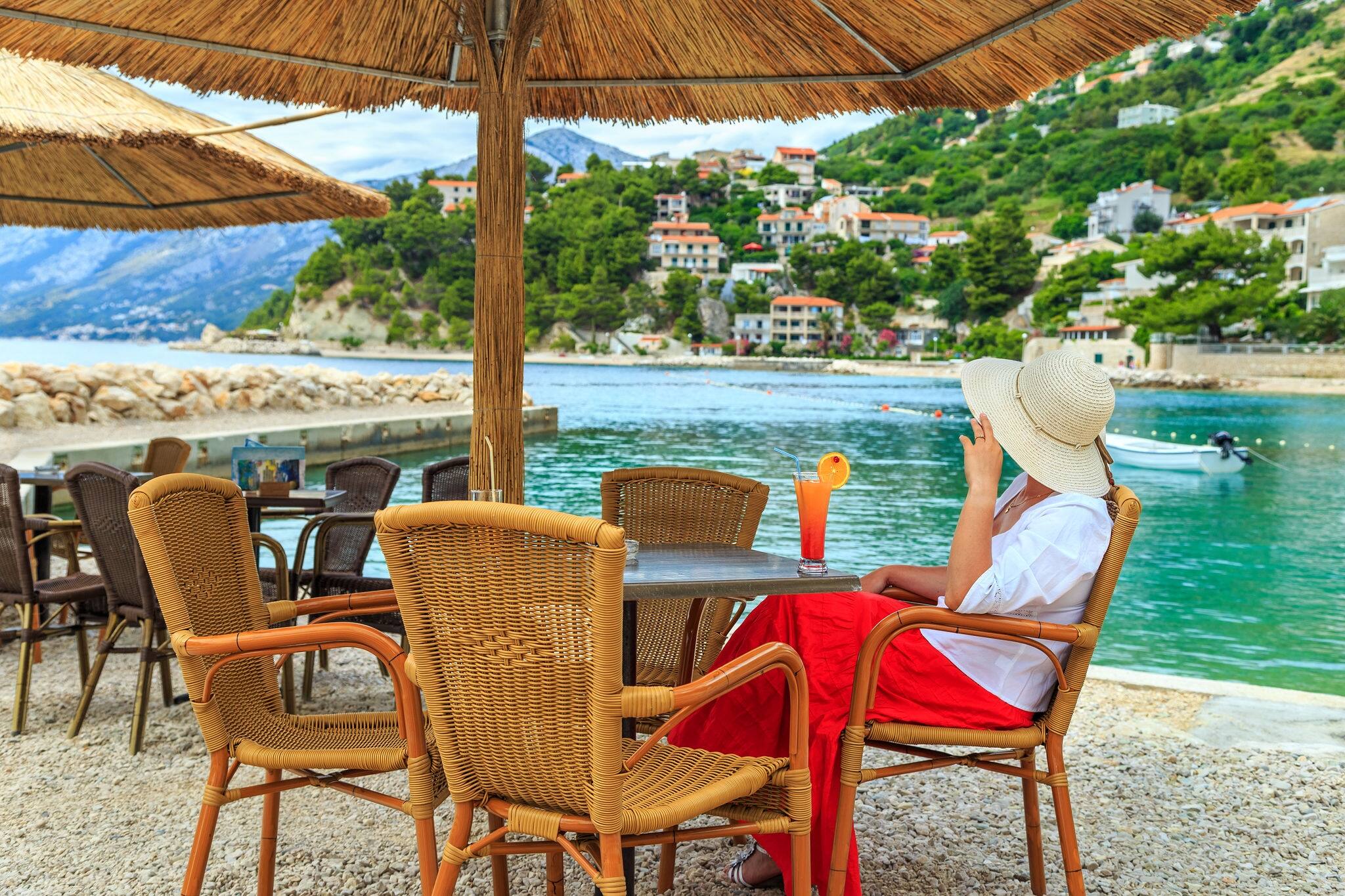 Stunning pretty woman sit in red skirt and white shirt with fruit cocktail on the beach