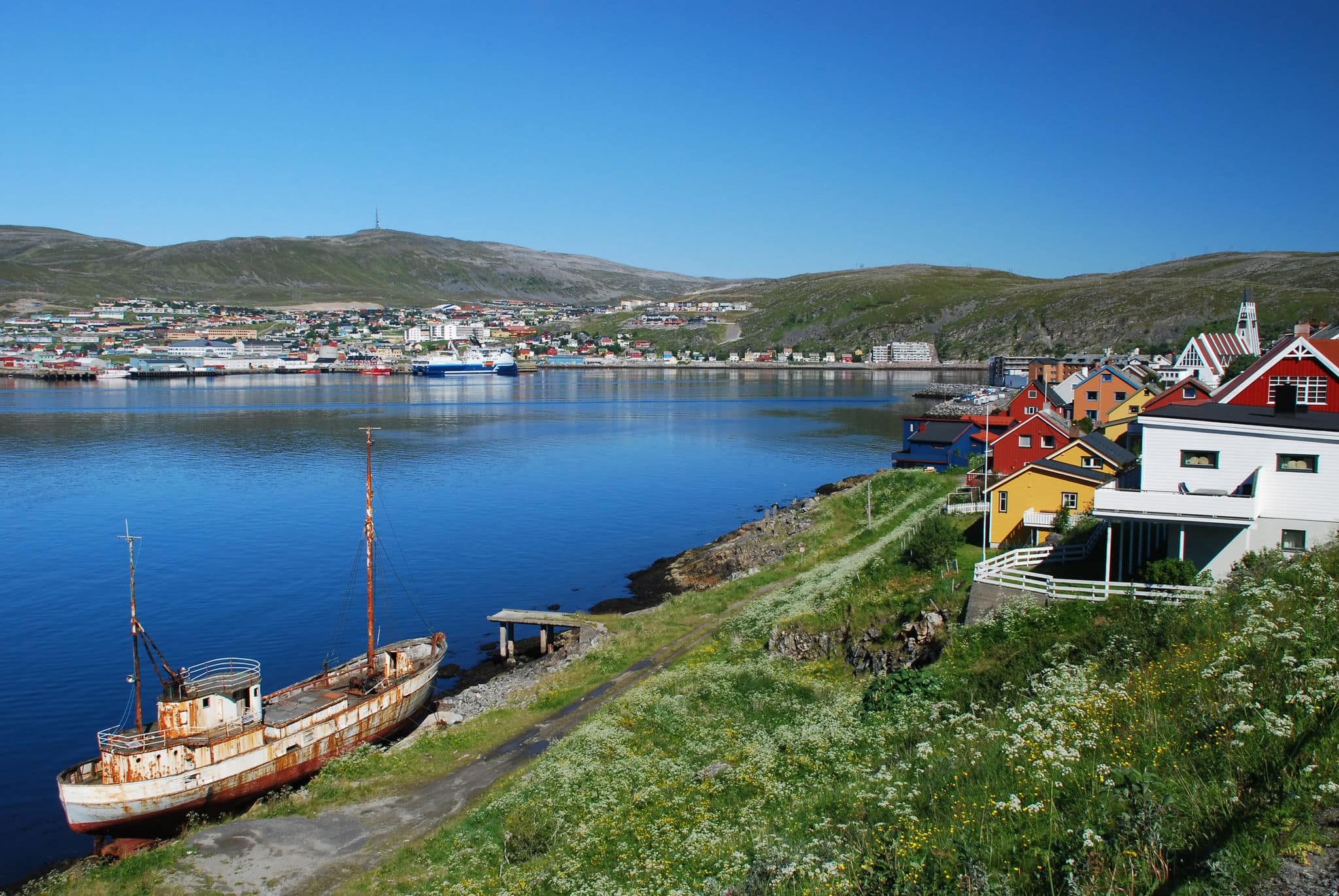 Its a cityscape of Hammerfest, claimed as a northernmost city in the world, the top of city church is behind of houses colored with colours of Finnmark country and old vessel in the border of see