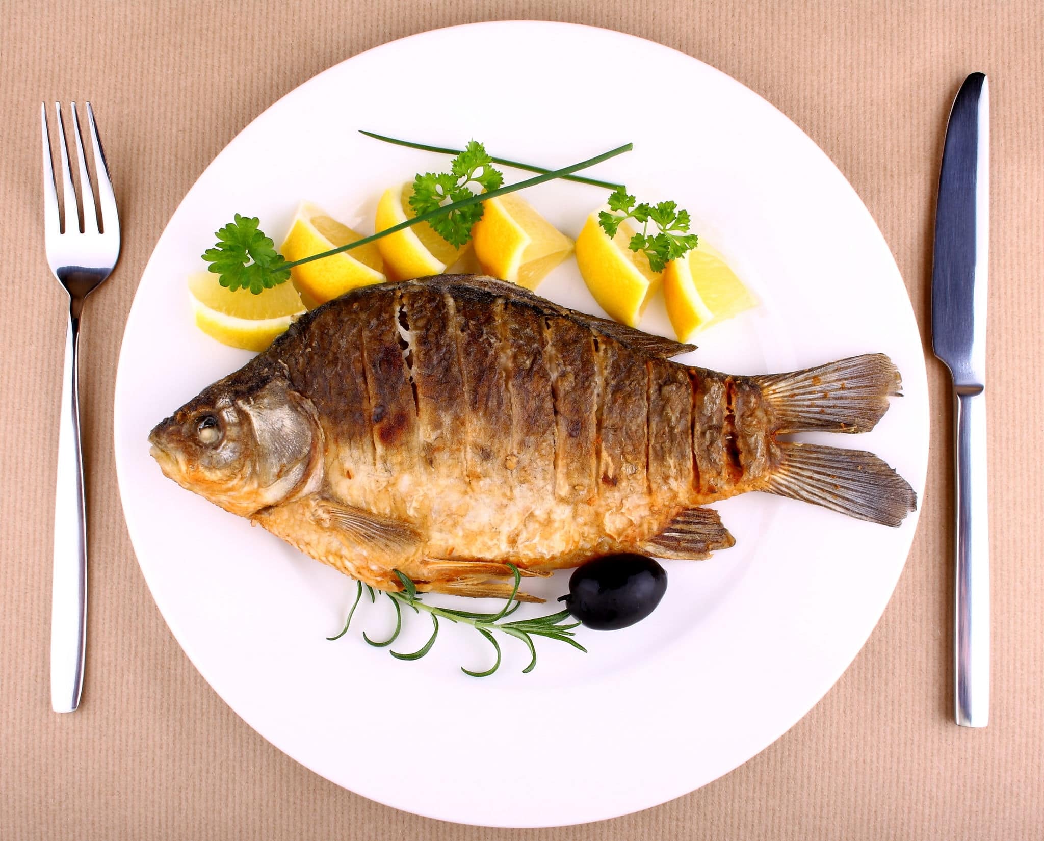 Fried fish on white plate with fork and knife, closeup