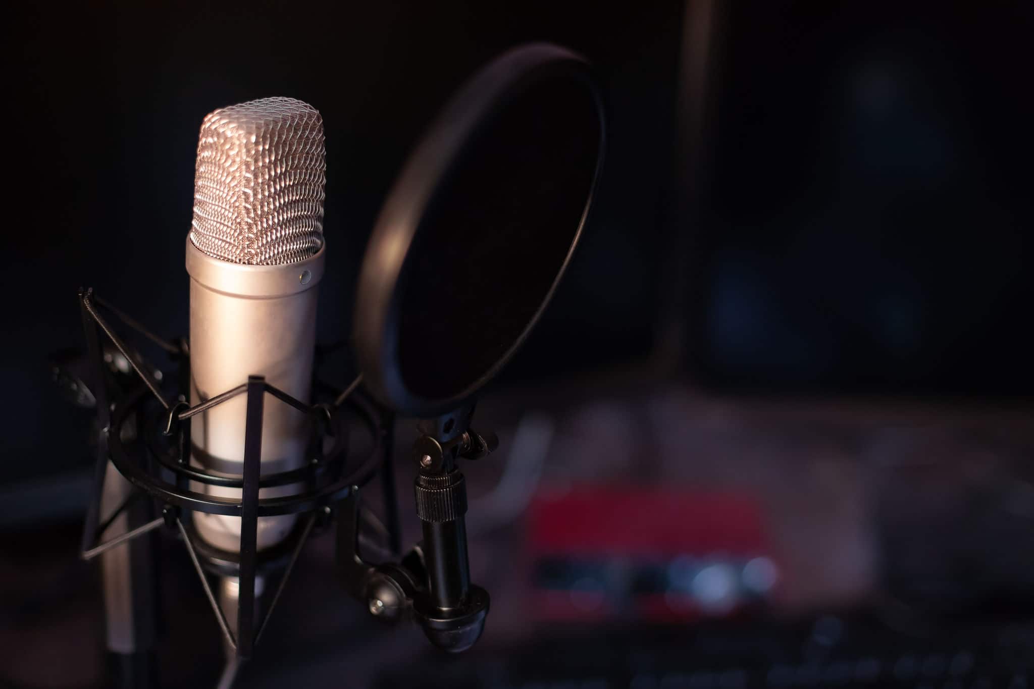 Silver studio microphone that stands out against the black background mounted with an anti-pop filter