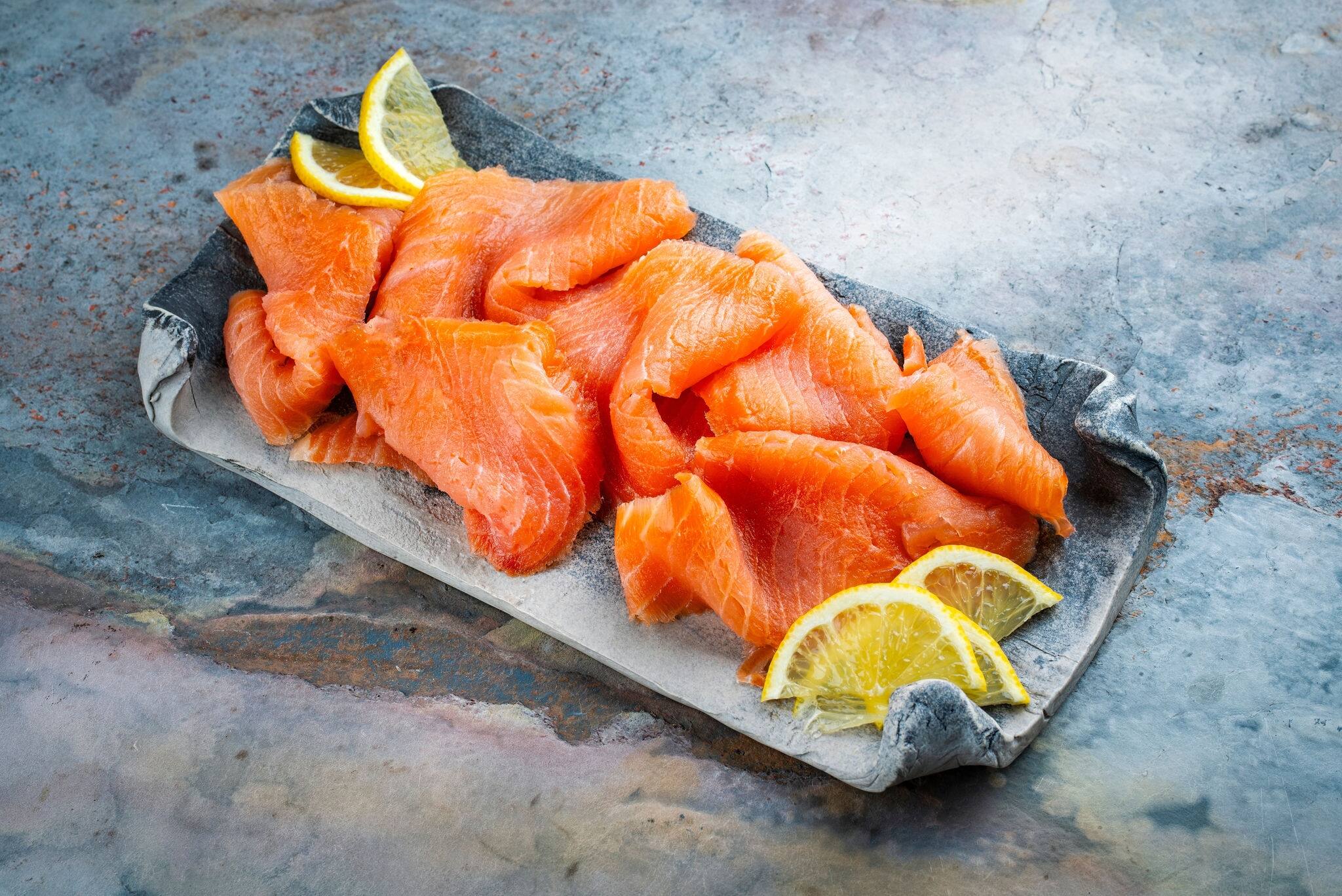 Traditional Norwegian smoked salmon in slices with lemon slices served as close-up on a Nordic design tray with text space 