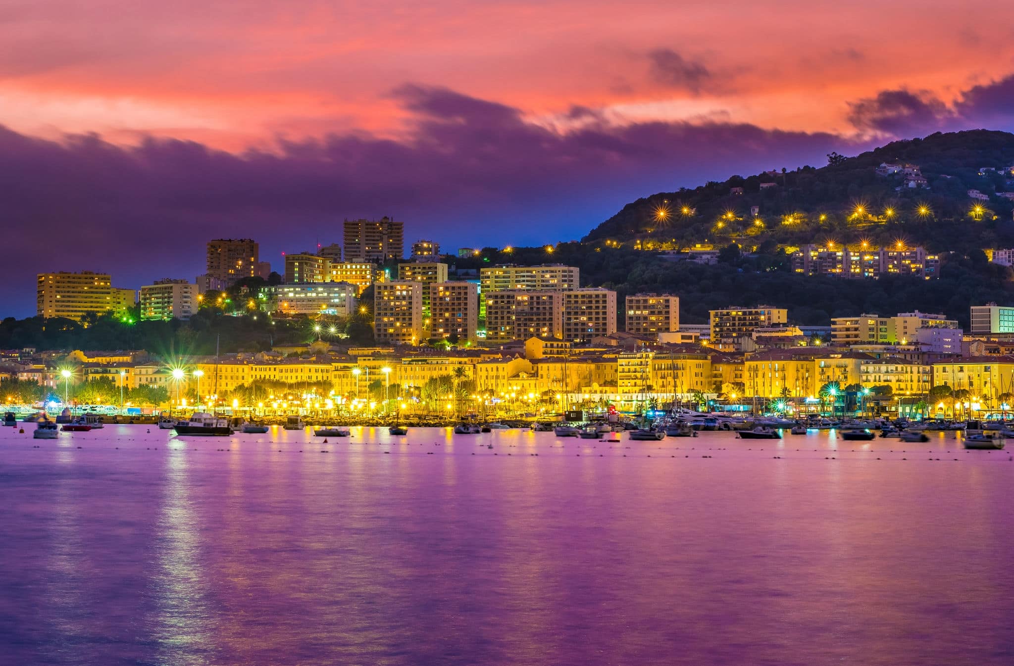 The evening in Ajaccio, big city skyline in the light of gorgeous purple sunset and reflection in water, Corsica, France.