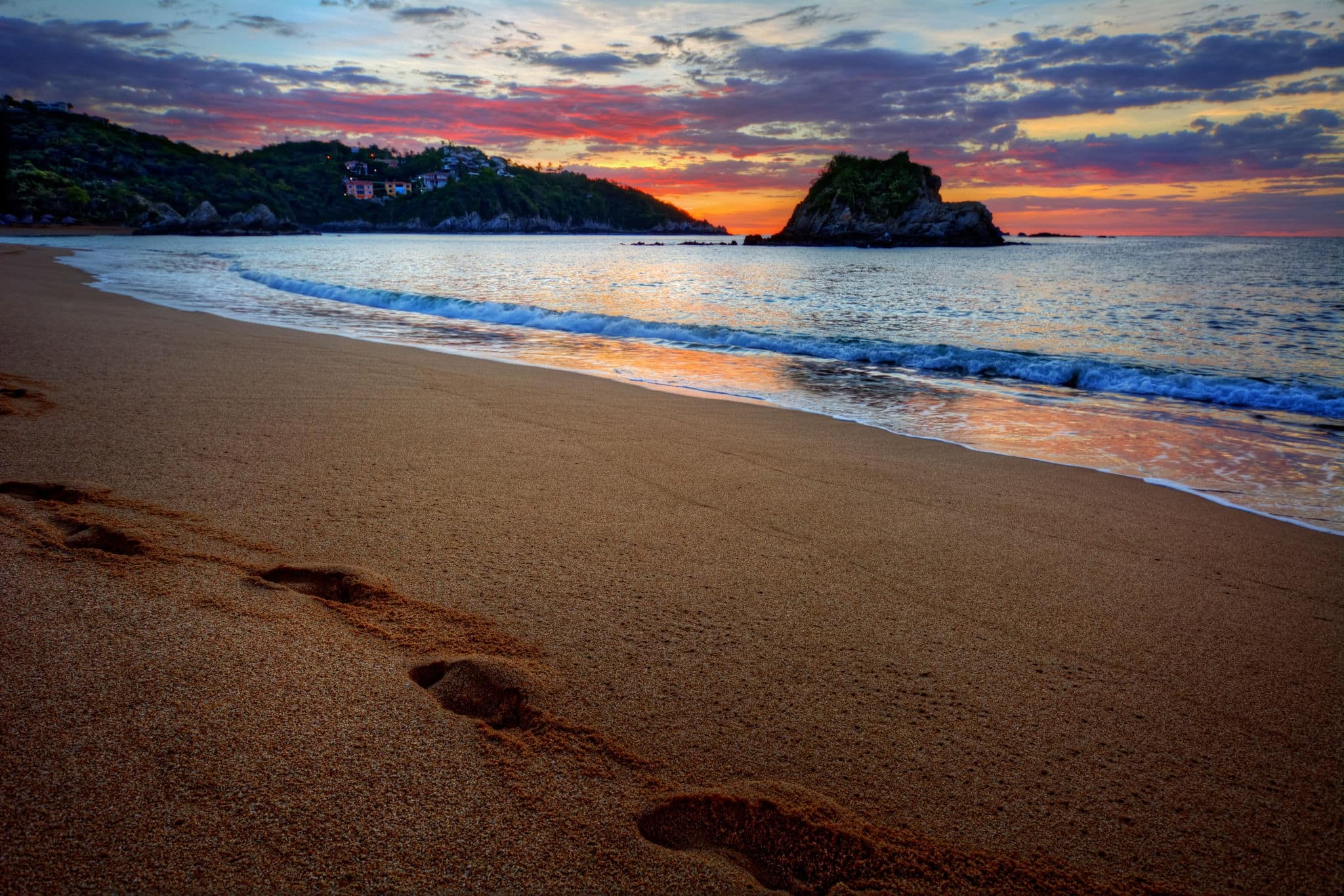 Foot prints along a beautiful sandy sea shore with distant hills at sunrise 