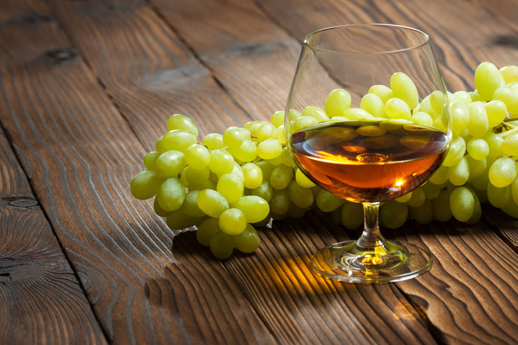glass of cognac and bunch of grapes on a wooden table.