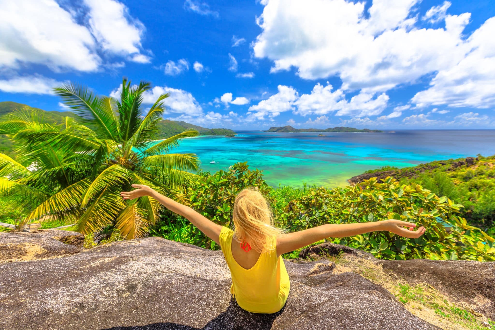 Top view panorama of Praslin, Seychelles. Carefree woman in yellow dress enjoying amazing views of Anse of Gouvernement overlooking Cote d'Or Bay with Curieuse, St Pierre and Chauvre Souris Island