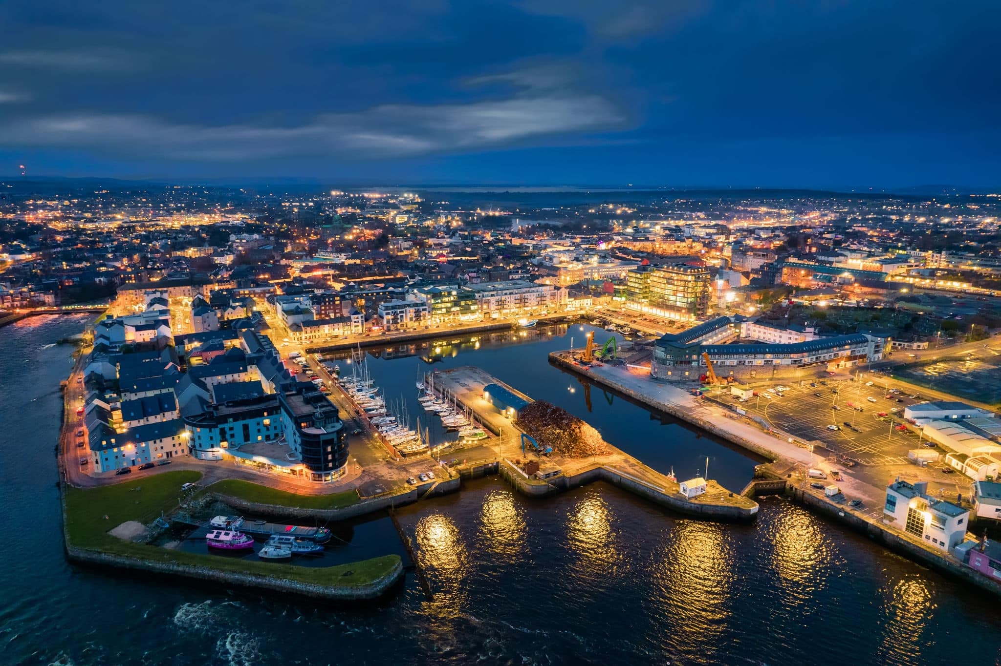Illuminated port town at night. Aerial view on River Corrib and Galway city, Ireland. Dark sky. Popular educational center and tourist hub with vivid night life.