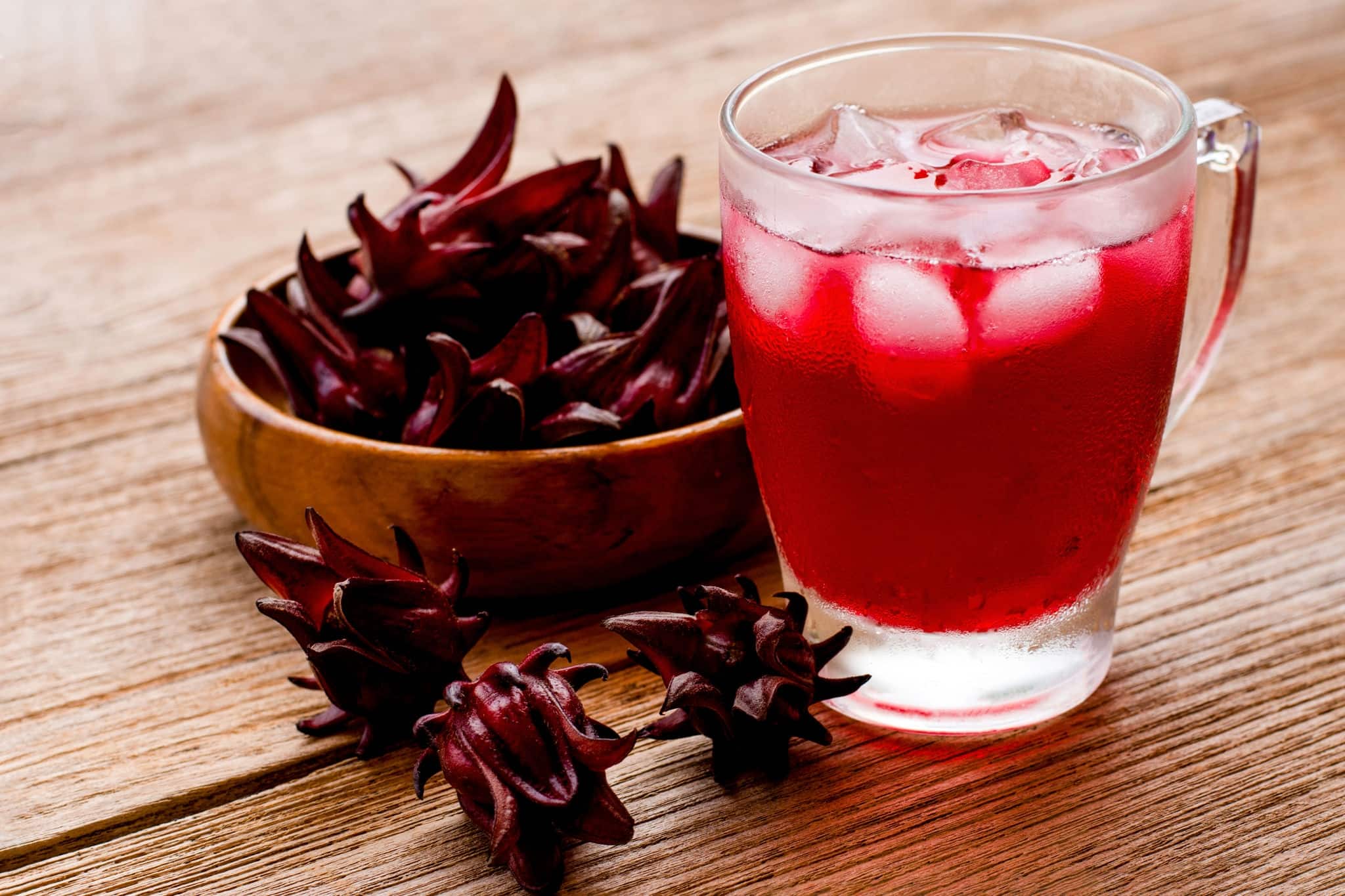 Closeup glass of roselle juice tea and  fresh red  Roselle fruit ( Jamaica sorrel, Rozelle or hibiscus sabdariffa ) isolated on old rustic wooden table background.