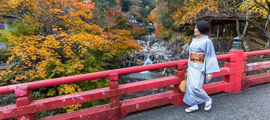 Woman in kimono, walking across bridge in Japan.