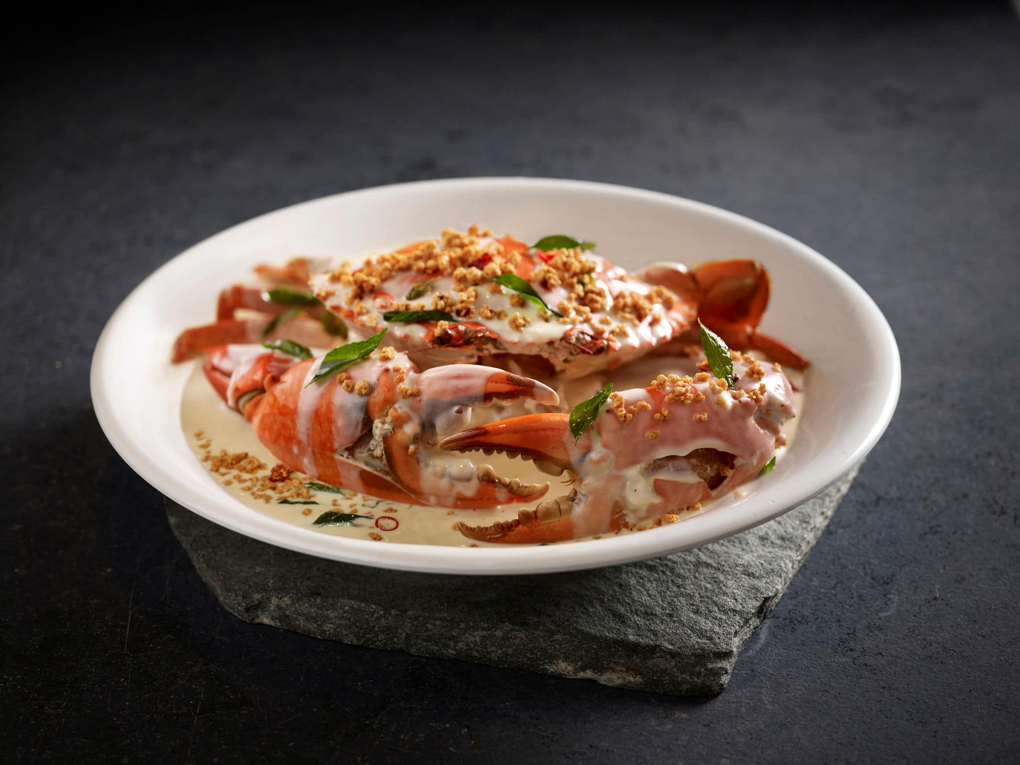 Signature Creamy Butter Sri Lankan Crab topped with Coconut Crumbs served in a dish side view on dark background