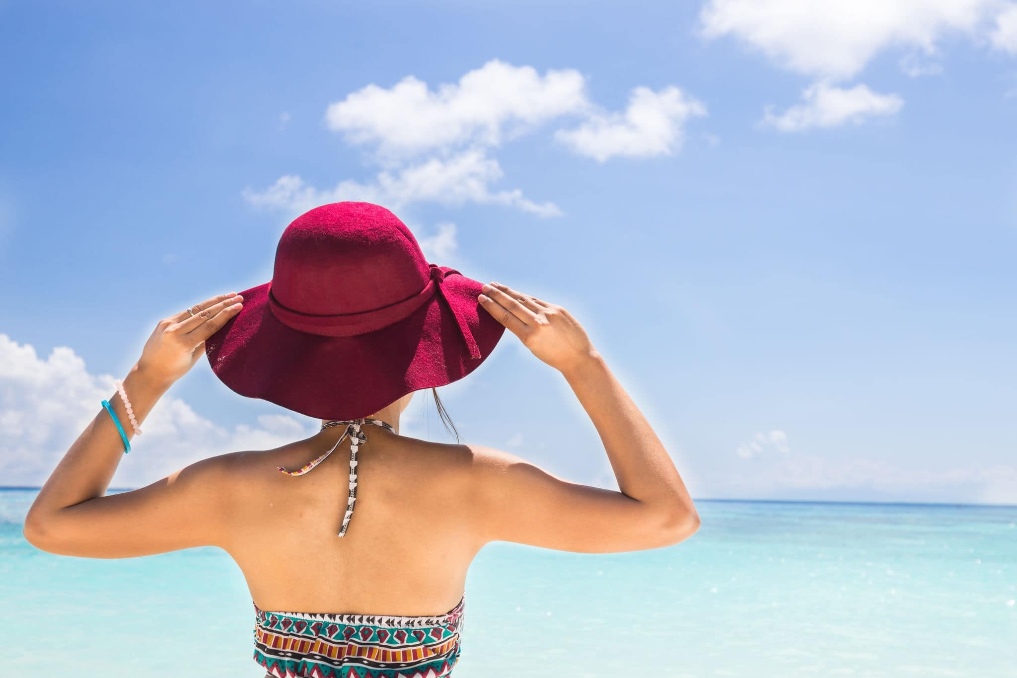 woman wear bikini stand on beach holding red beach hat enjoying summer holidays looking at the ocean