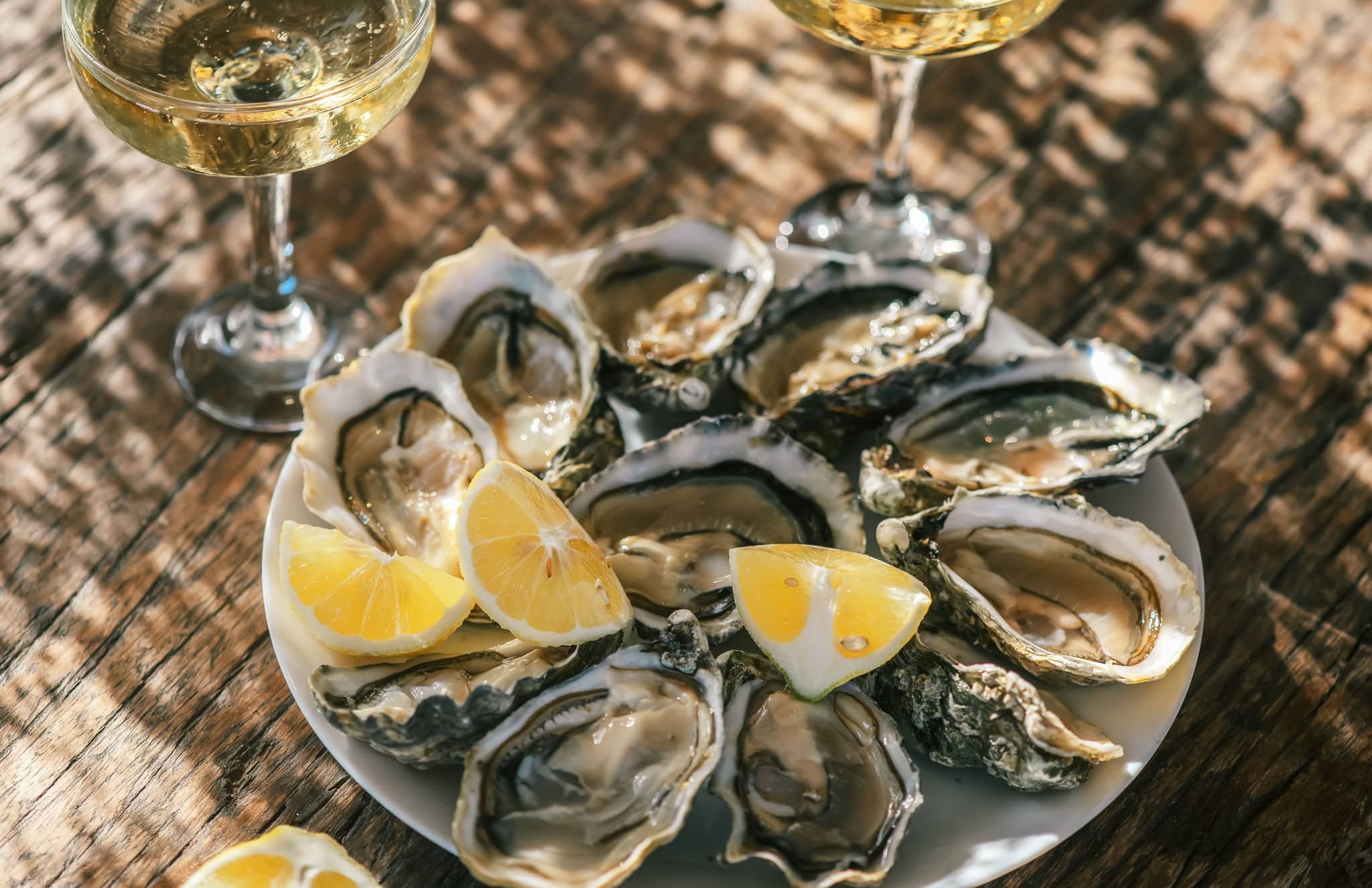 Fresh Oysters with champagne close up top view, over wood background, open french Fine de Claire oysters. Dinner in a restaurant, sea food. Served table with Oyster. Gourmet food, delicatessen  