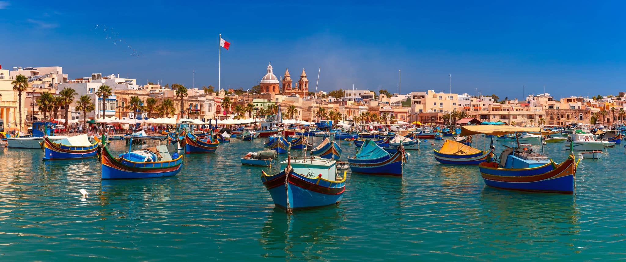 Panorama with traditional eyed colorful boats Luzzu in the Harbor of Mediterranean fishing village Marsaxlokk, Malta