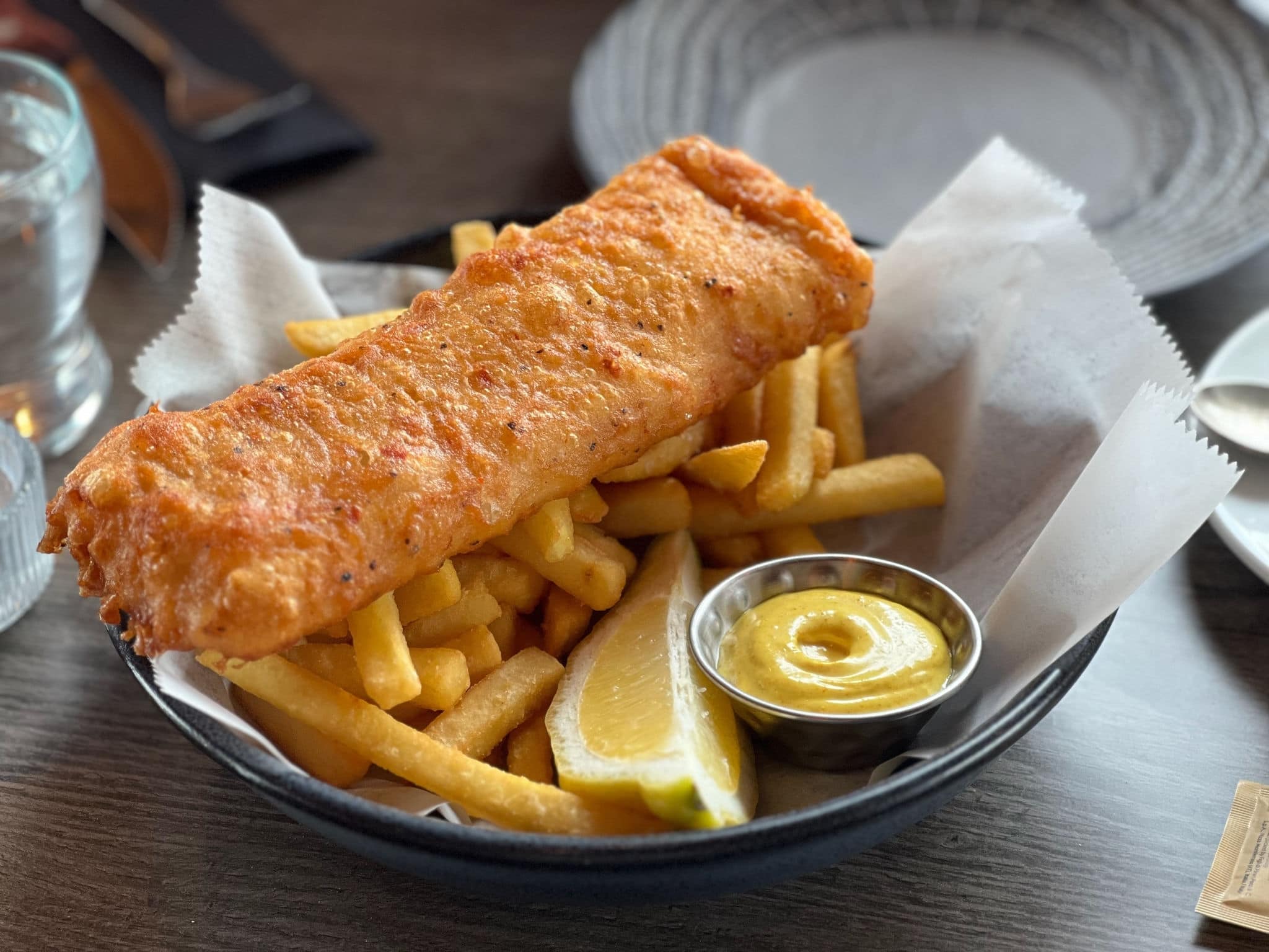 A plate of deep-fried cod fish and chips with a lemon slice and sauce tartare