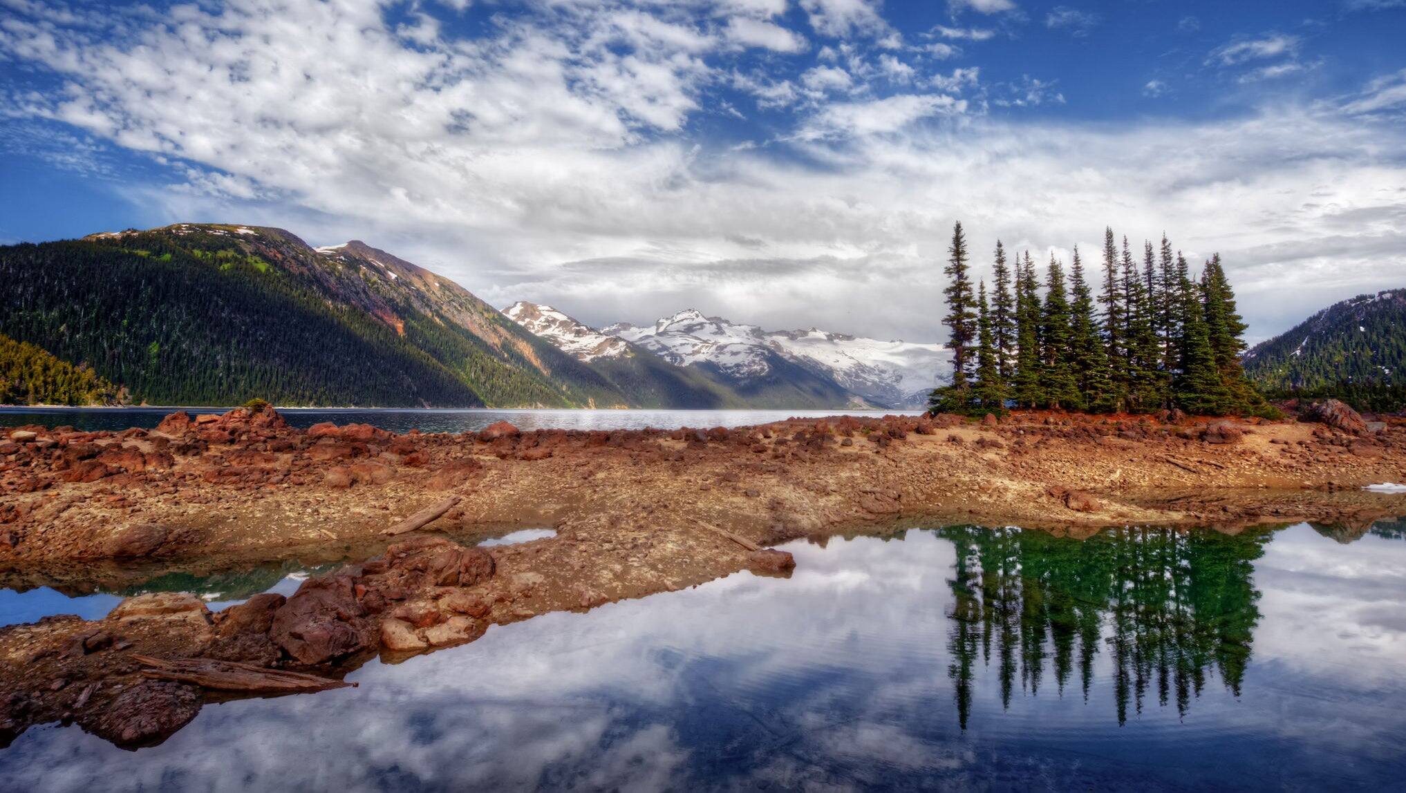 Glacial mountain lake with red blooming flowers, blue sky and dark cliffs